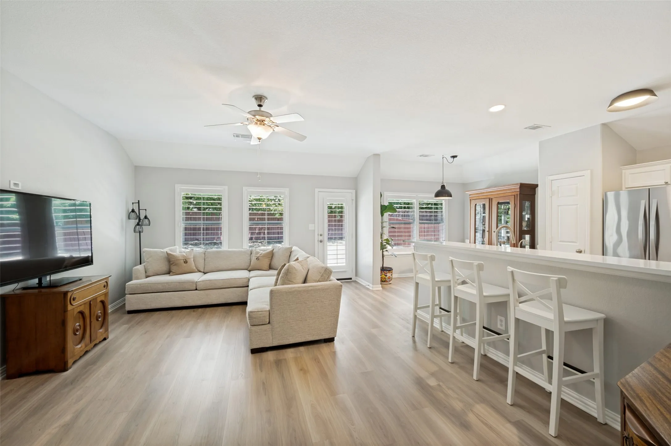 Expansive room featuring wood-finish flooring, a ceiling fan with light fixture, and multiple windows with plantation shutters