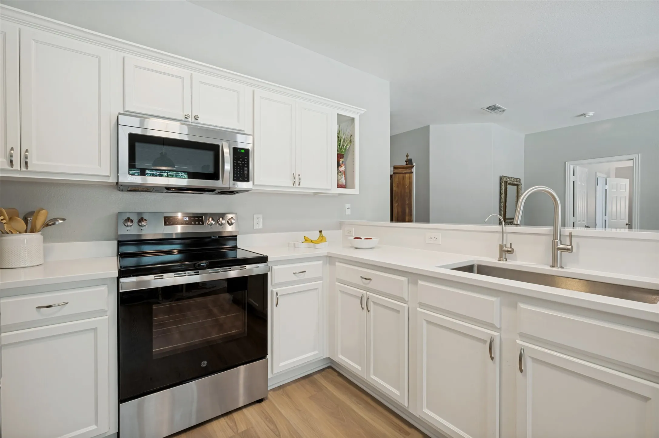 Contemporary kitchen featuring white cabinetry with brushed nickel hardware, stainless steel appliances including a built-in wall oven and microwave, quartz countertops, and a spacious island with an undermount sink and chrome pull-down faucet