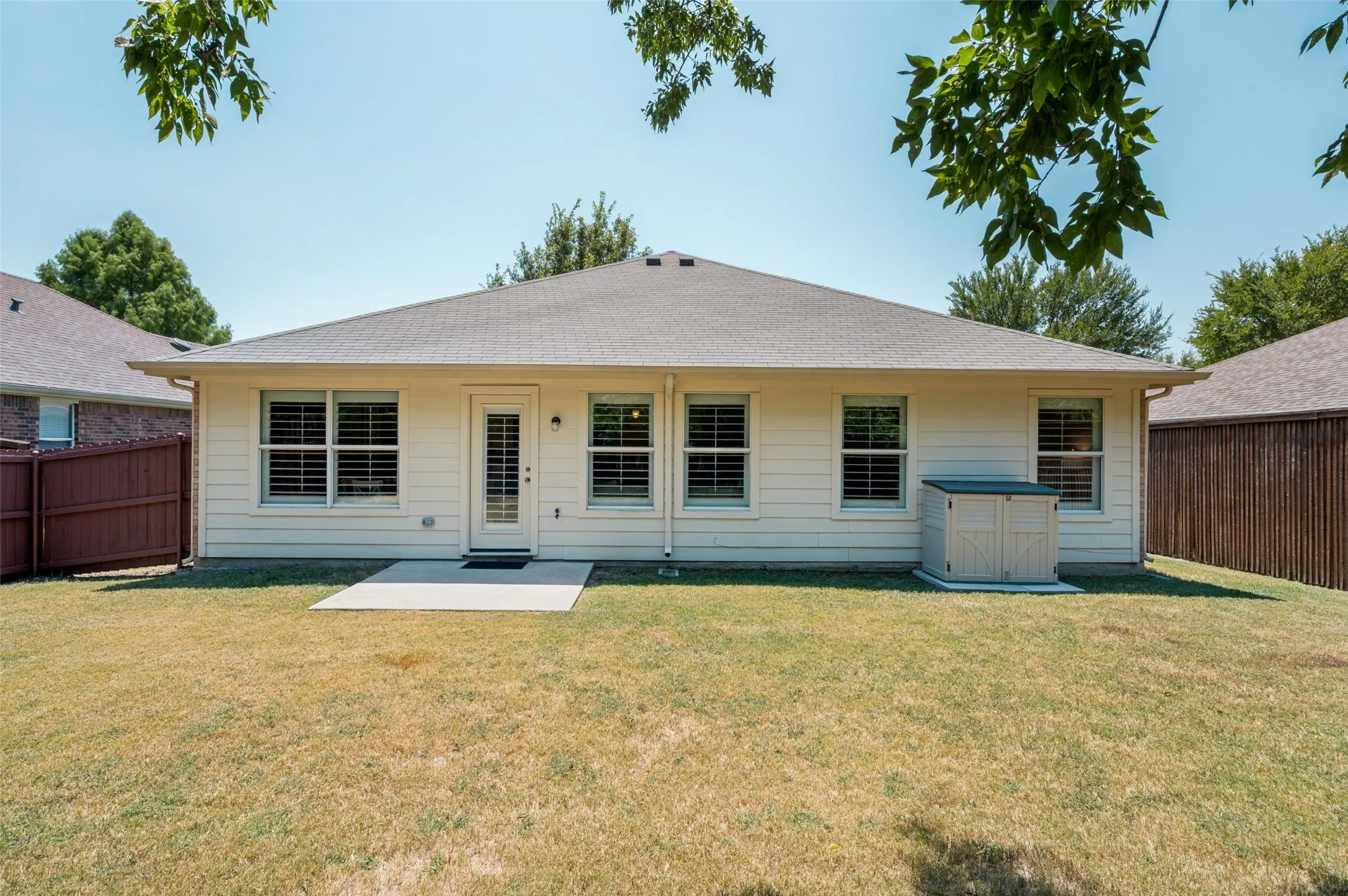 Expansive rear yard featuring a concrete patio, exterior siding, multiple windows with shutters, and a storage shed