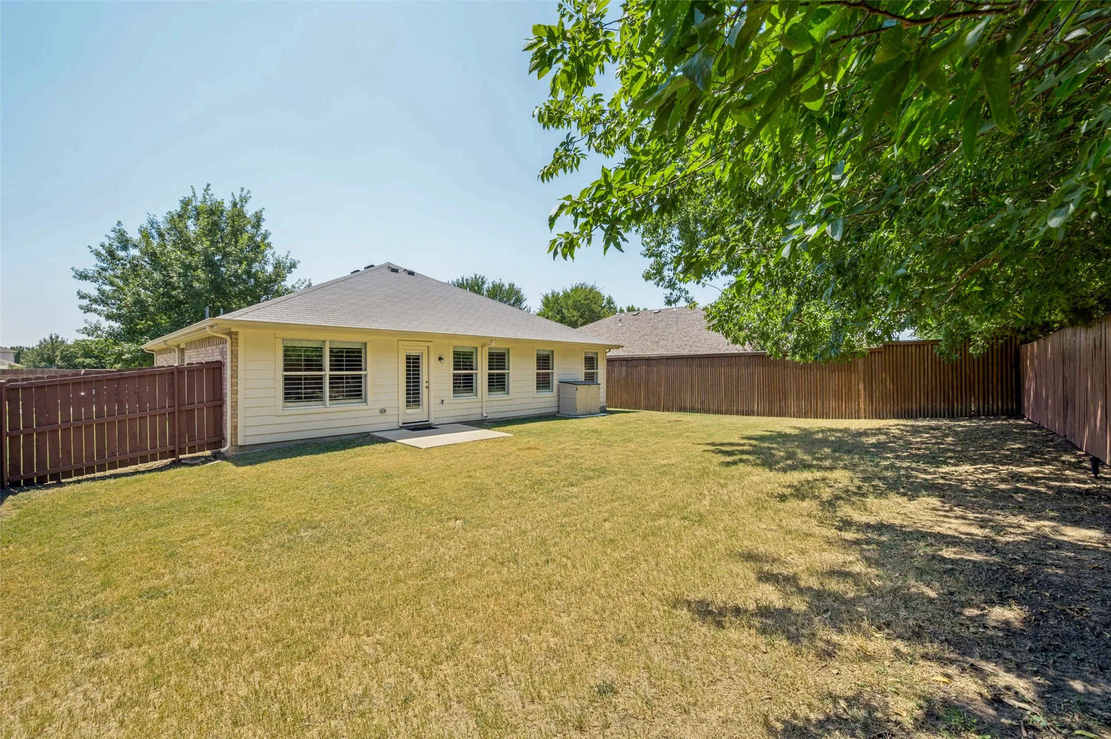 Expansive backyard featuring a concrete patio, wood fencing, and mature trees