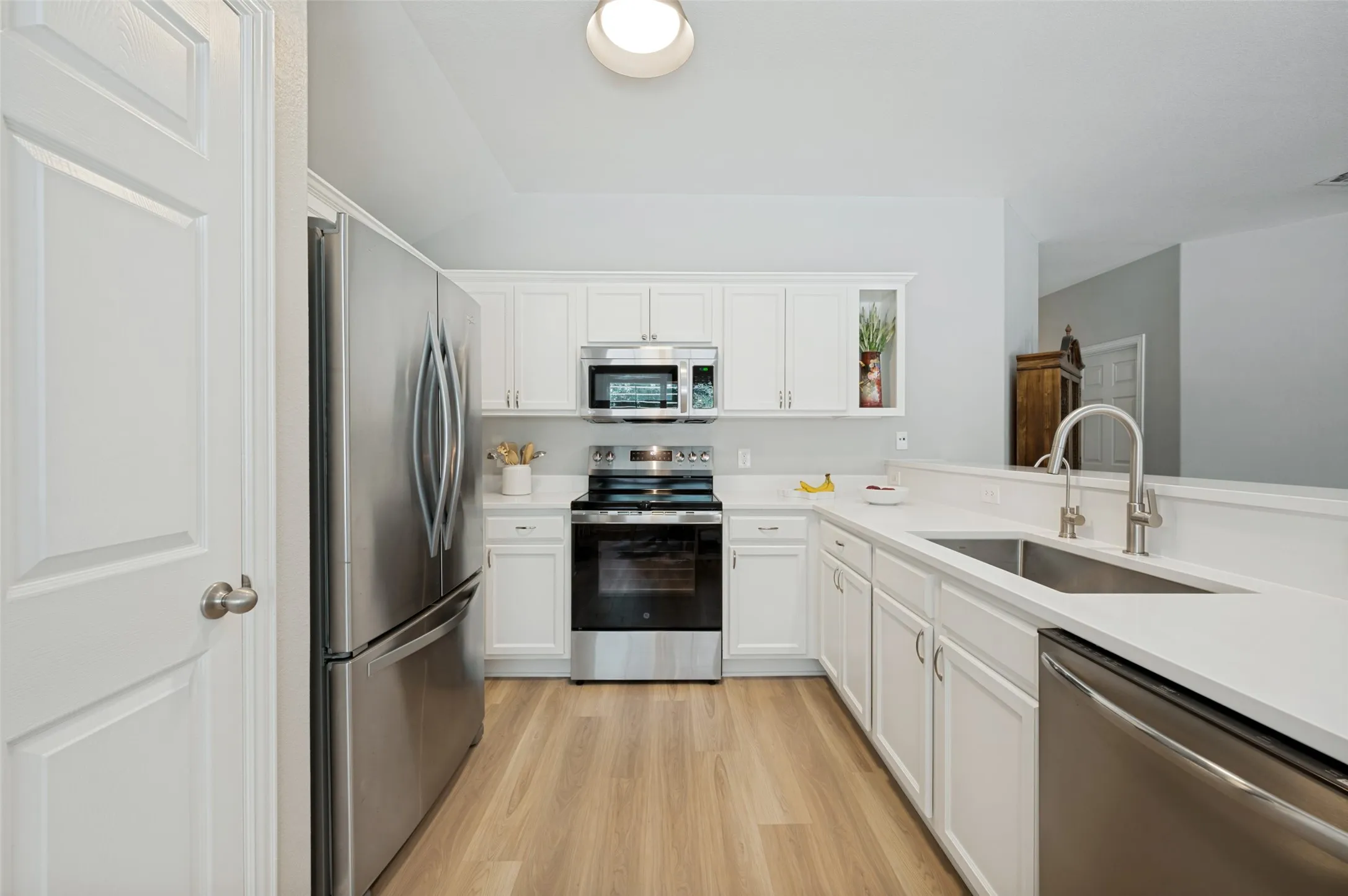 Kitchen featuring white cabinetry, stainless steel appliances, light-toned countertops, a dual basin sink, and wood-finish flooring