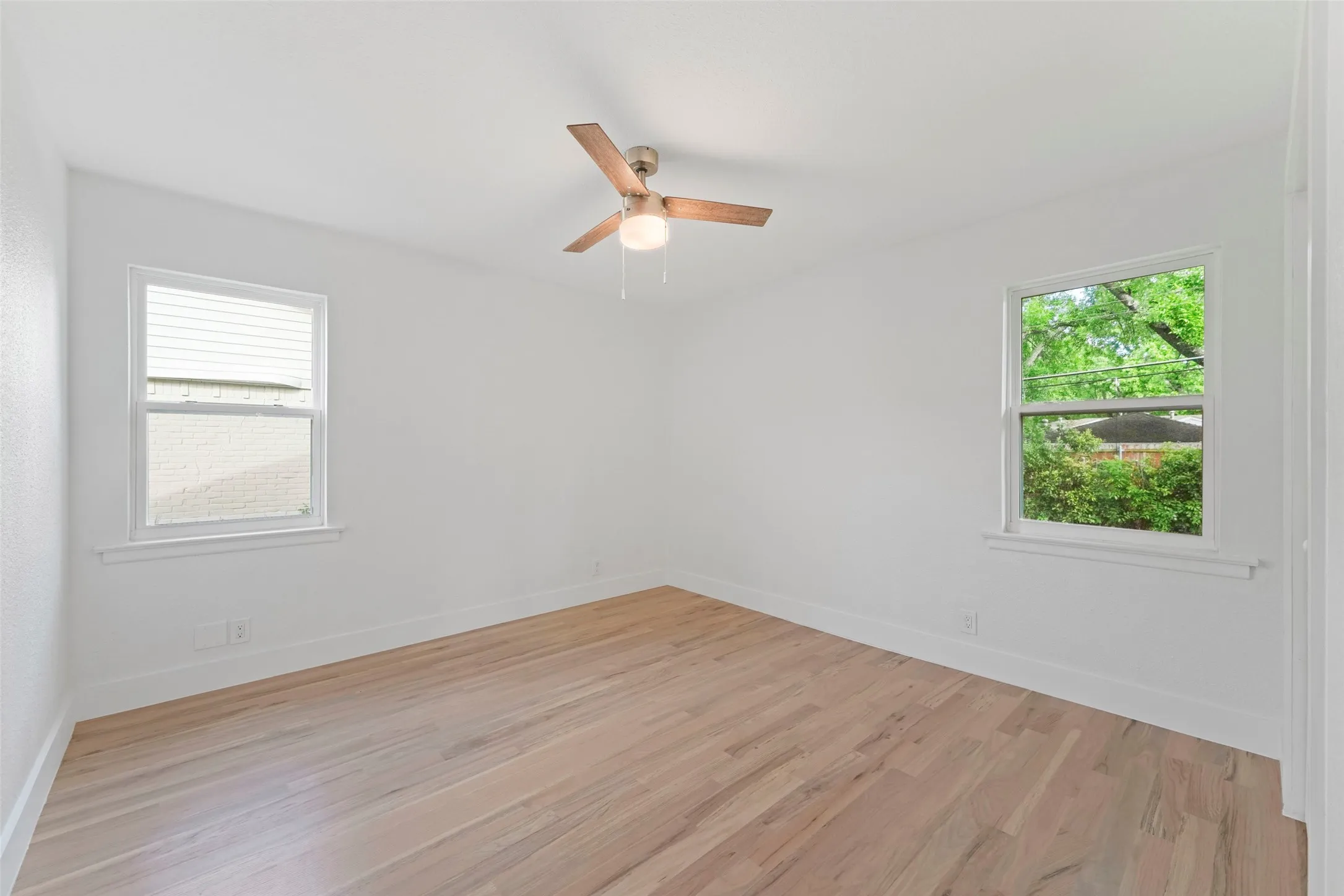 This room features light-colored hardwood flooring, white walls, and a ceiling fan with wooden blades