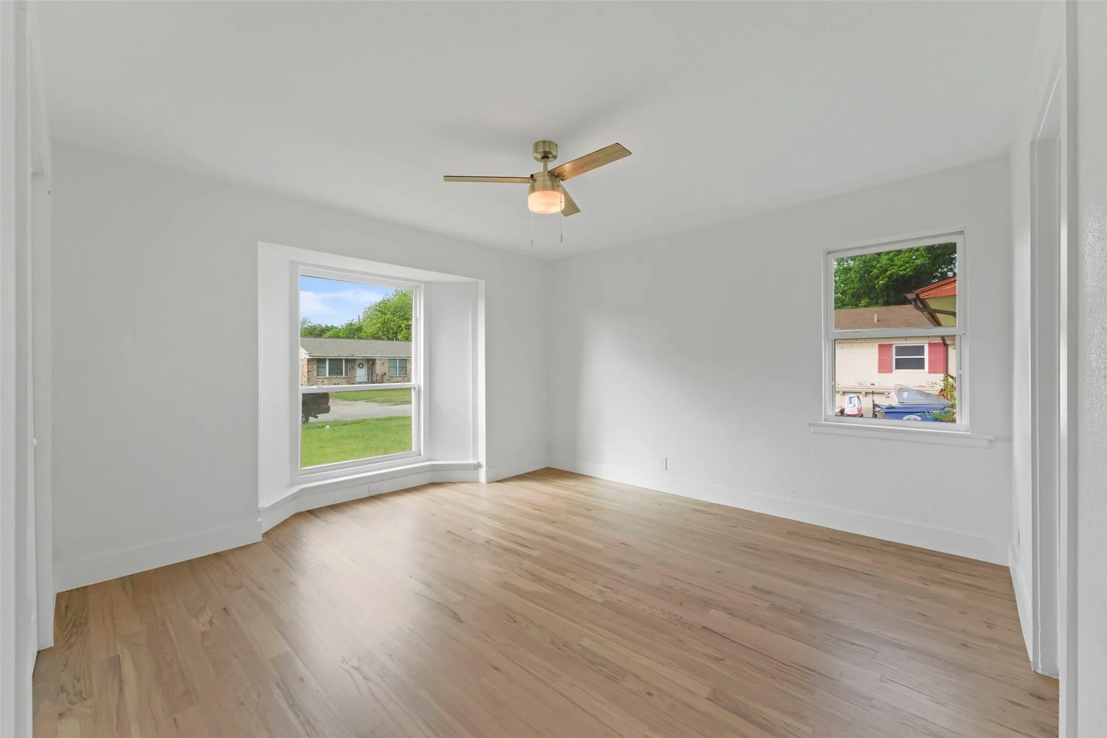Spacious room featuring light-colored flooring, white walls, a ceiling fan, and multiple windows providing natural light