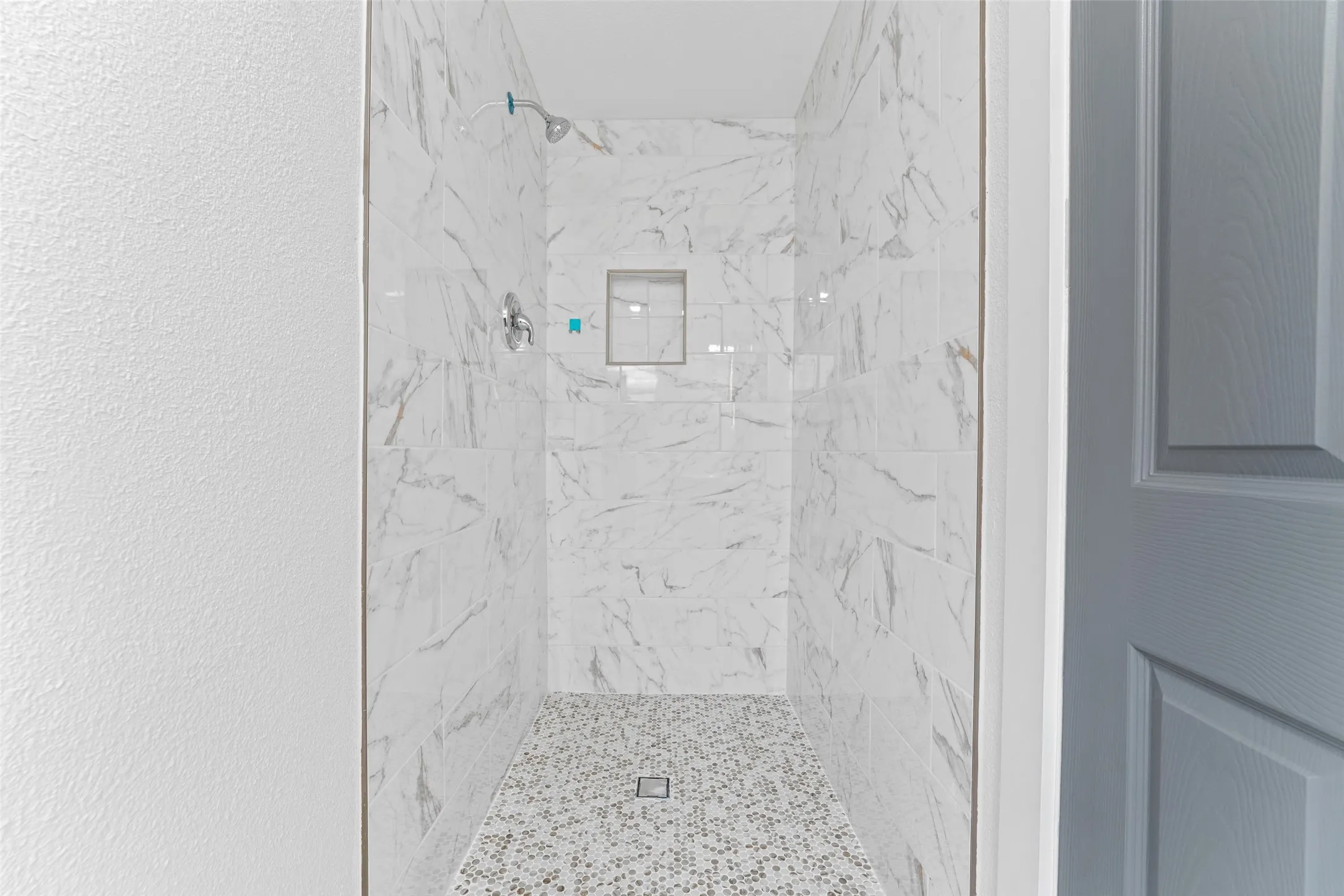 The shower features white marble-look tile walls, a mosaic tile floor, and a built-in shower niche