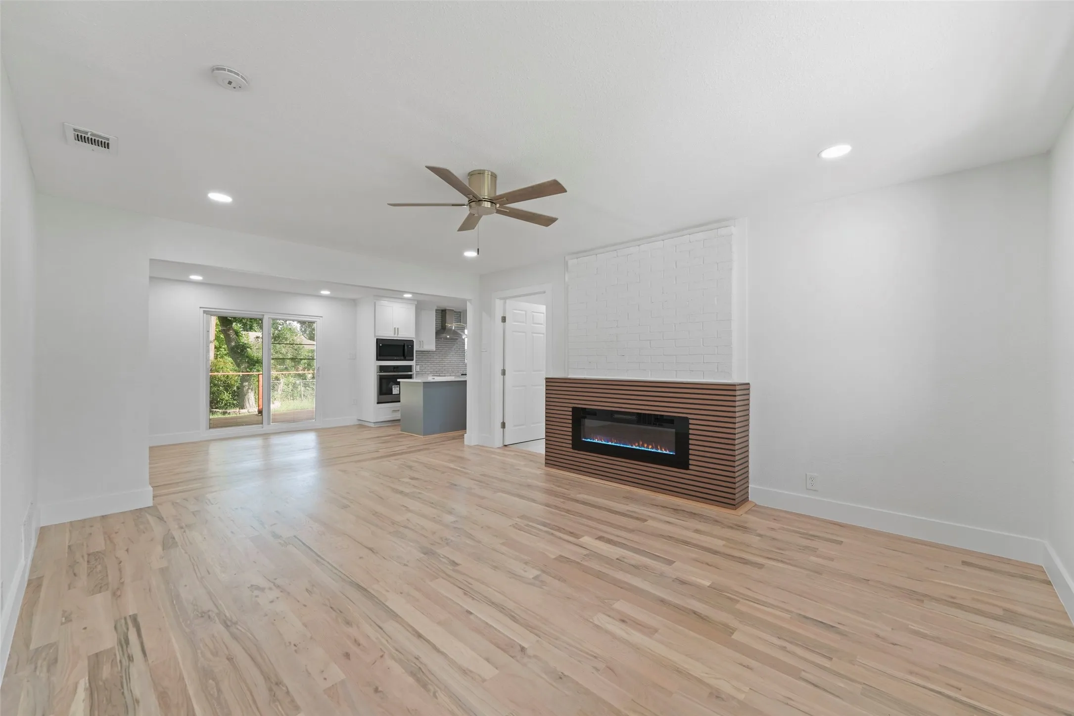 Spacious living area featuring light wood flooring, an electric fireplace with a slatted wood surround, and recessed lighting
