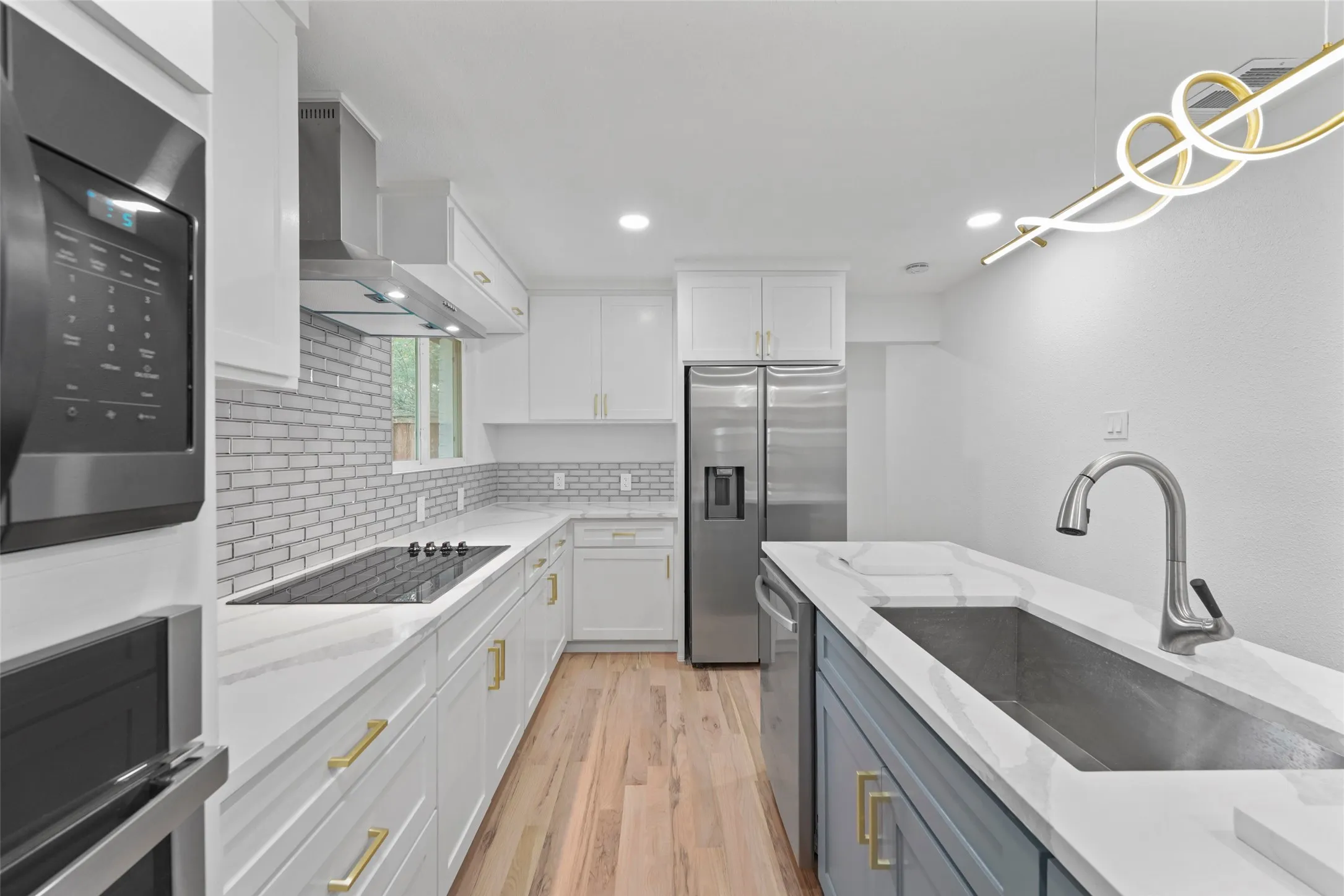 The kitchen features white shaker style cabinetry, stainless steel appliances, a modern backsplash, and light wood flooring