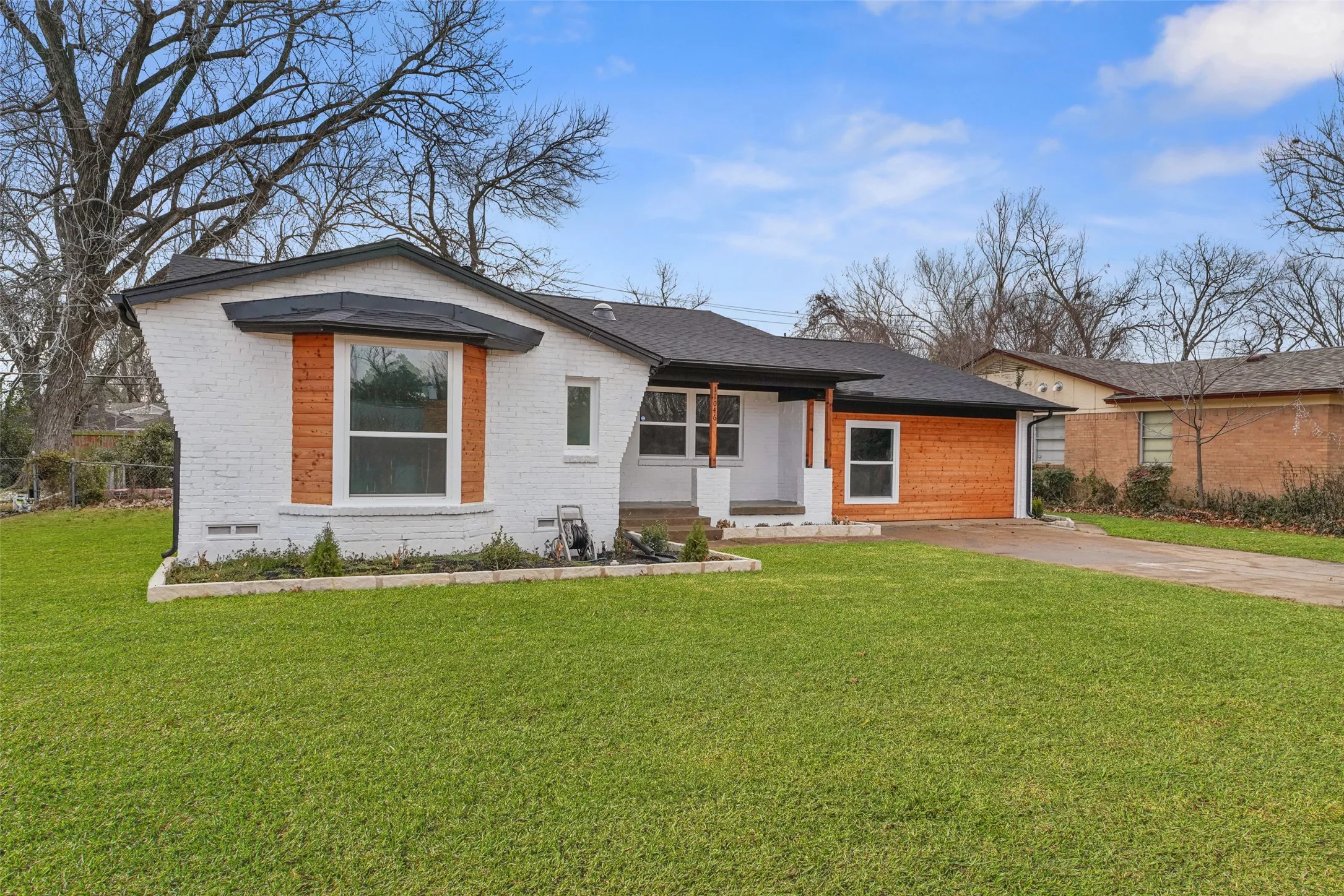 The property features a well-maintained lawn, a paved driveway, and a white brick exterior with wood paneling accents
