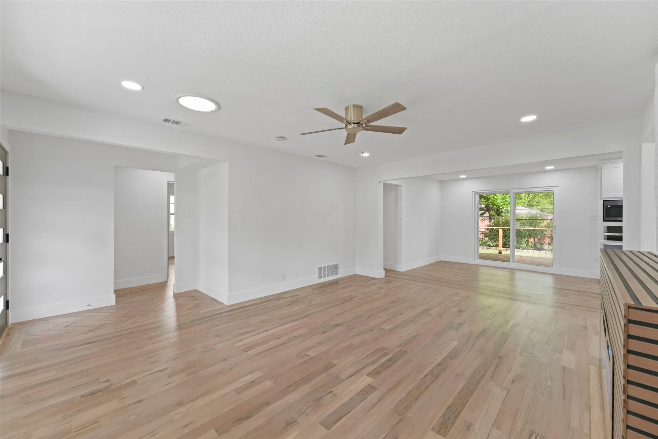 The expansive living area features light-toned wood flooring, recessed lighting, and a ceiling fan