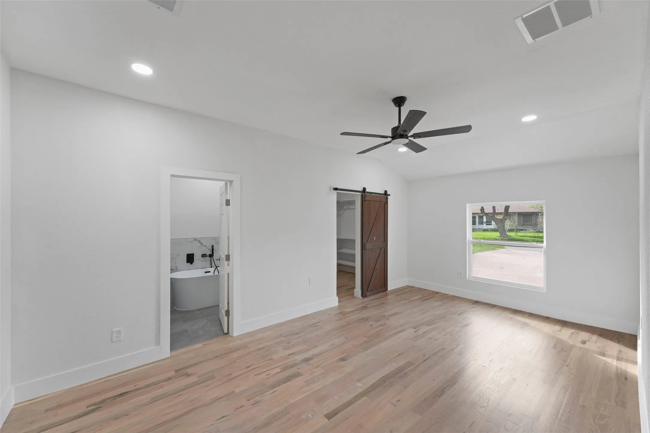 Spacious room featuring light wood flooring, a window, and a ceiling fan