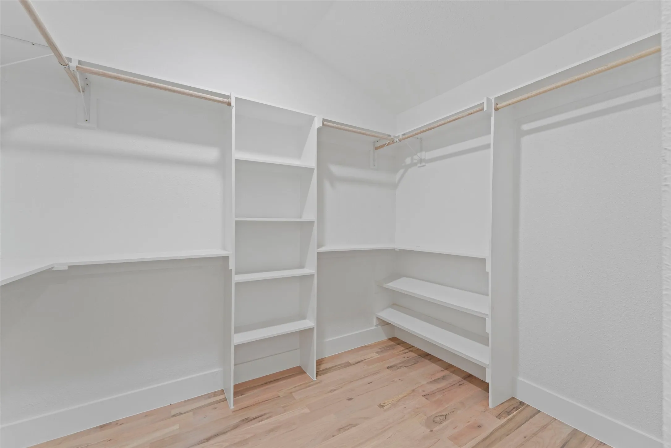 Expansive closet featuring light wood flooring, white shelving units, and hanging rods