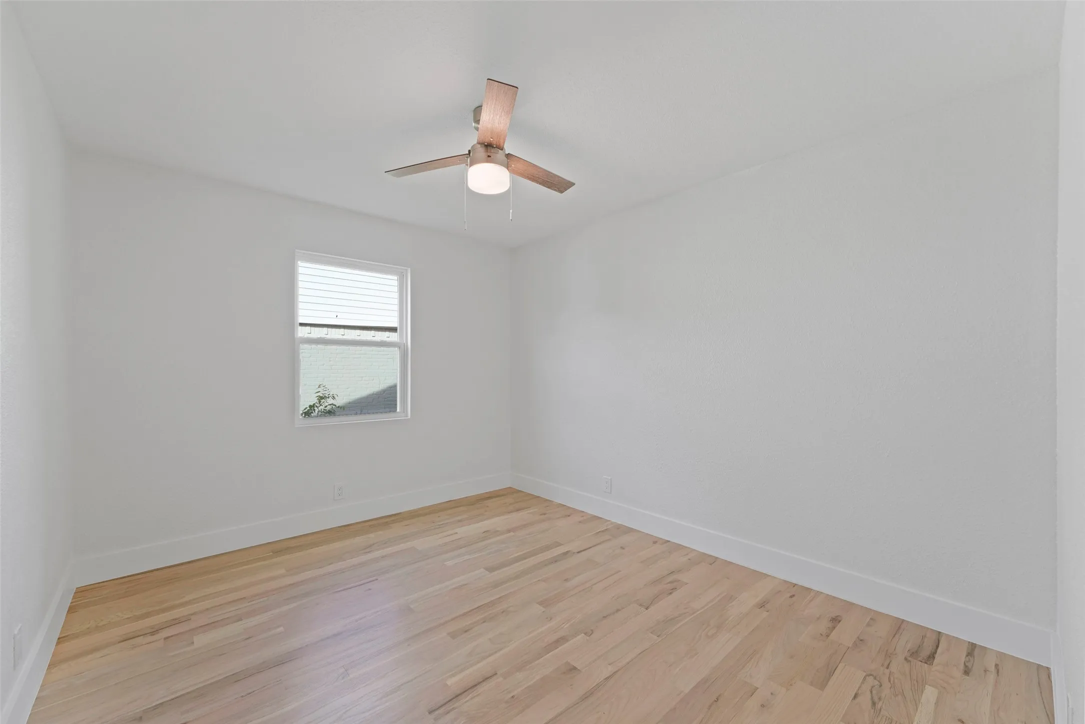This room features light hardwood flooring, white walls, and a ceiling fan with an integrated light fixture