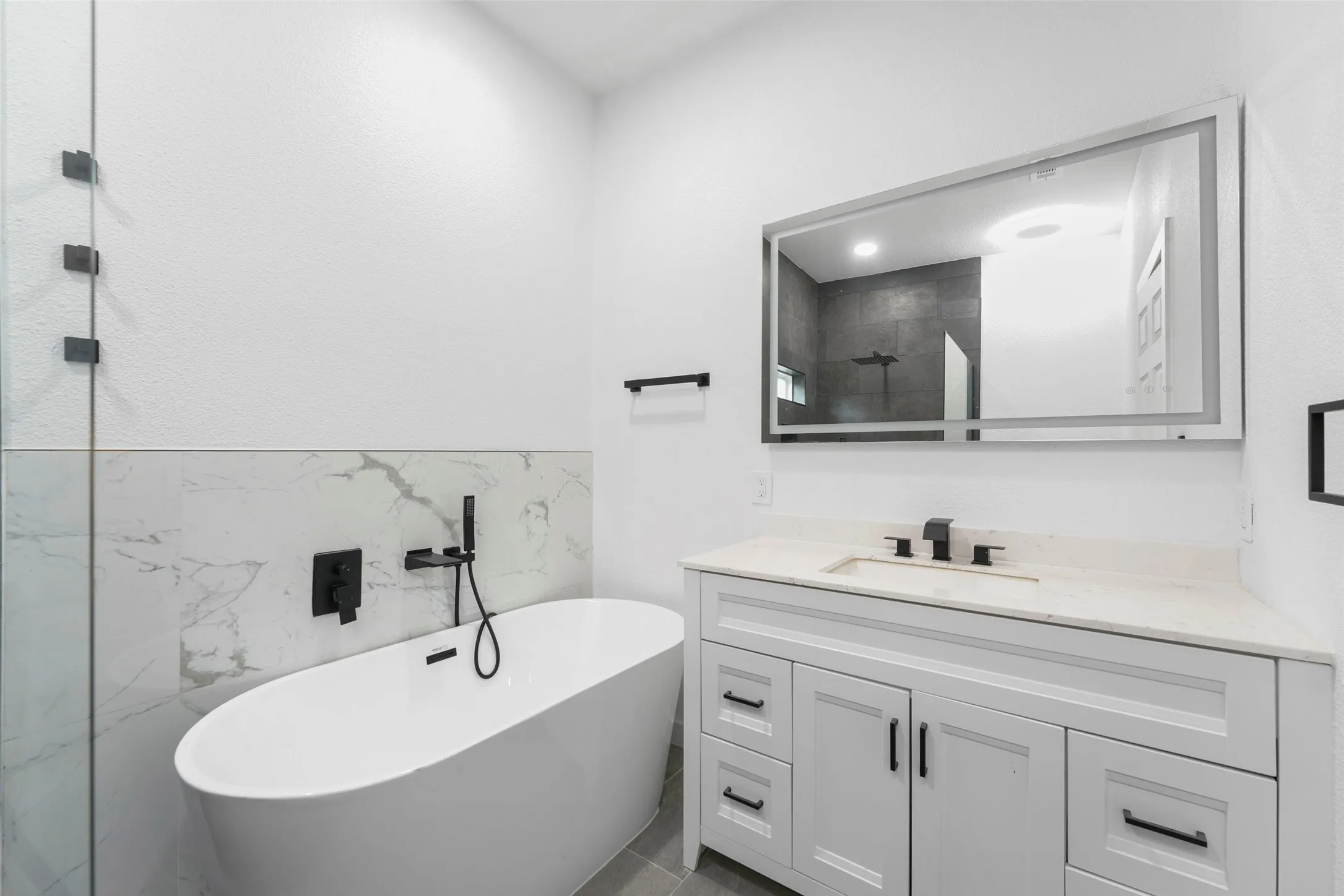 Bathroom featuring a freestanding oval bathtub, white vanity with a light-colored countertop, and a large rectangular mirror