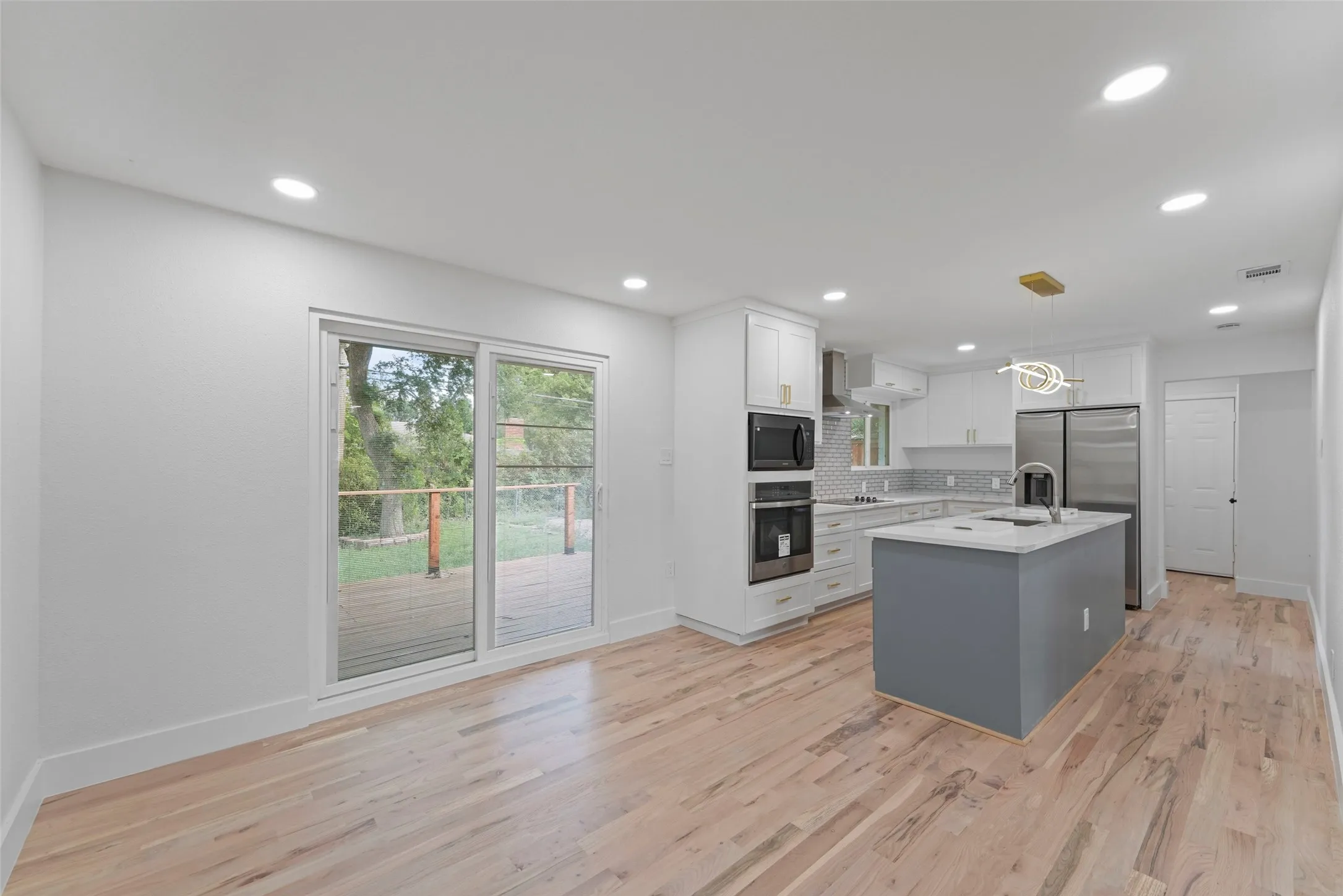 The property features hardwood floors, recessed lighting, and a kitchen with white cabinetry, a center island, stainless steel appliances, and a tiled backsplash