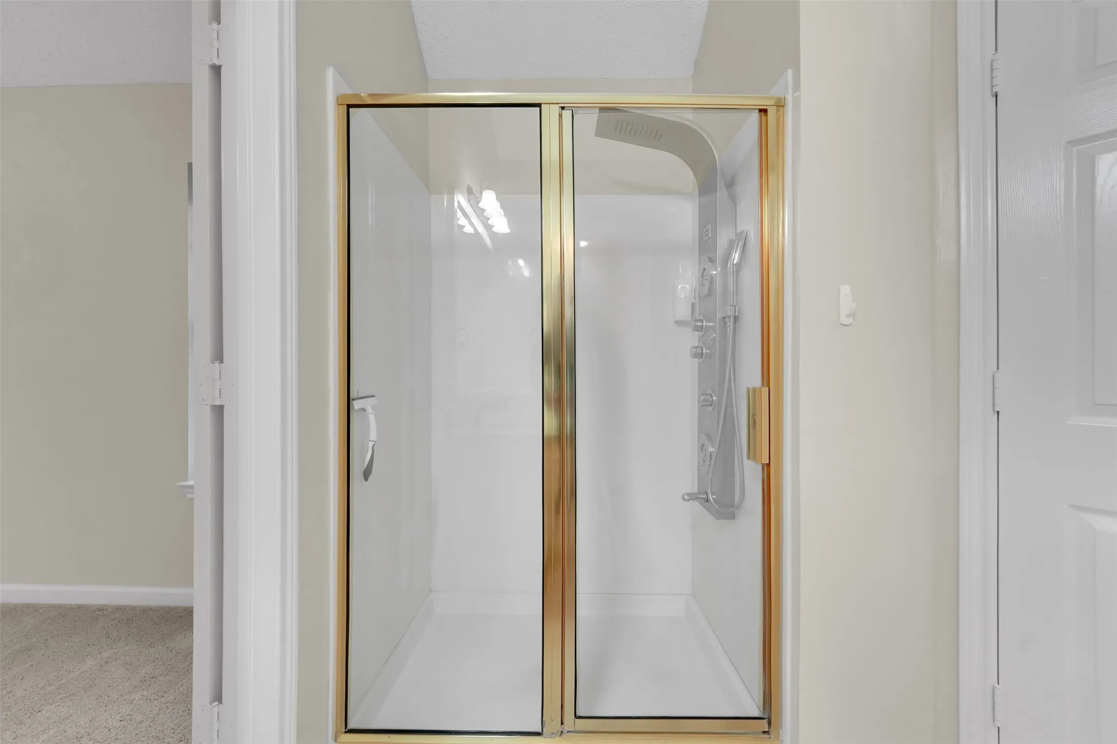 Frameless glass shower enclosure with brushed brass hardware and clean sightlines, positioned within a bright, neutral bathroom featuring white subway tile surround and soft natural lighting