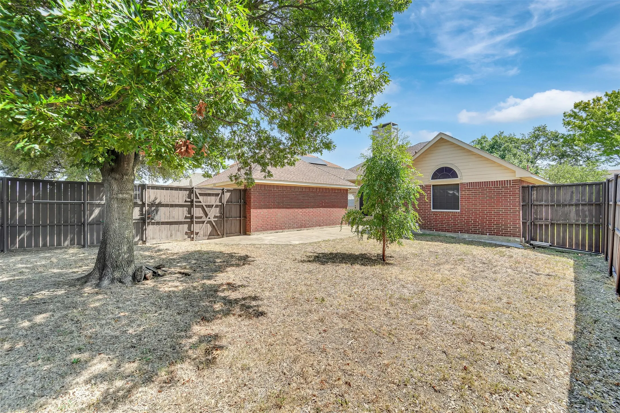 Fenced backyard with mature trees, brick exterior, and an arched window detail
