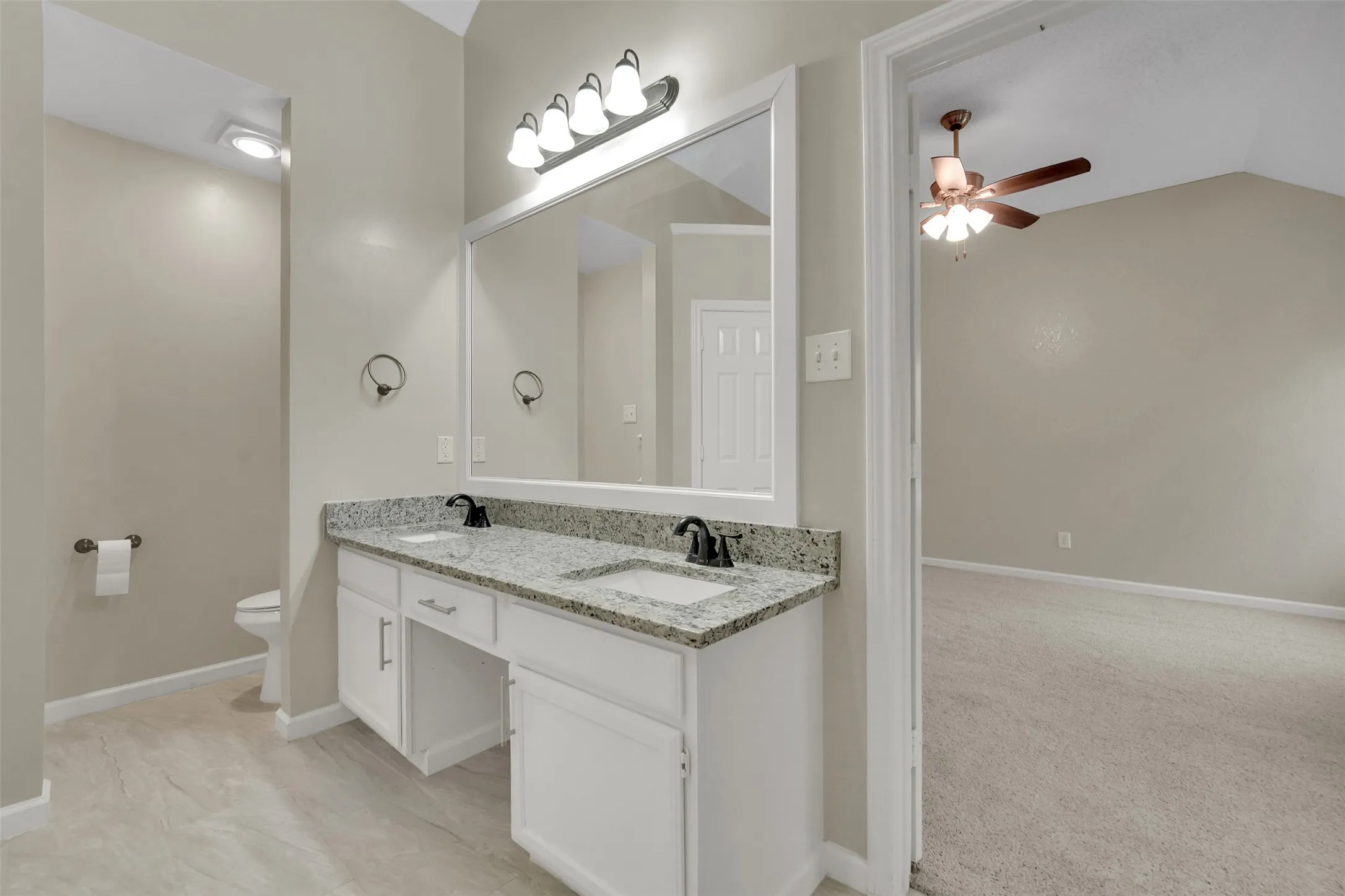 Primary bathroom featuring a dual-sink vanity with granite-style countertop, white cabinetry, and polished chrome fixtures