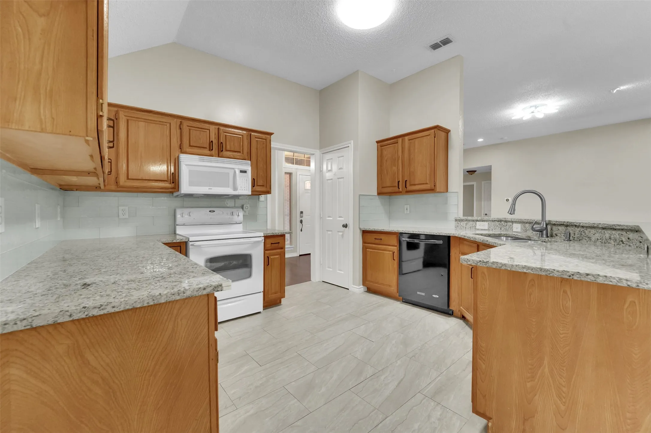 Spacious kitchen featuring warm wood cabinetry, granite countertops, stainless steel appliances, light wood-finish flooring, and recessed ceiling lighting throughout the open layout