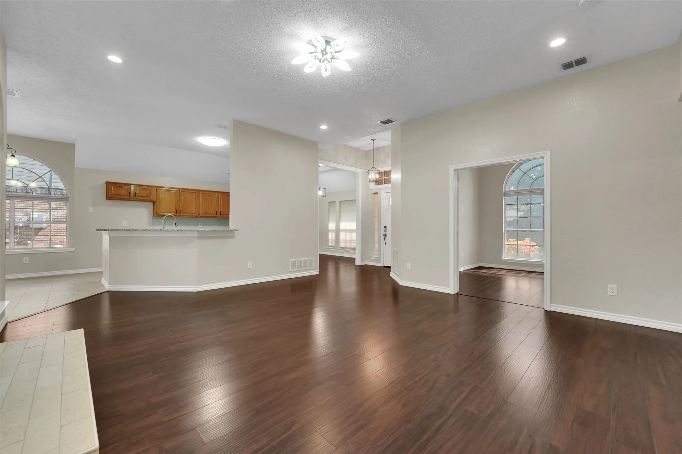 Spacious interior featuring wood-finish flooring, recessed lighting, arched windows, and a kitchen pass-through with a breakfast bar