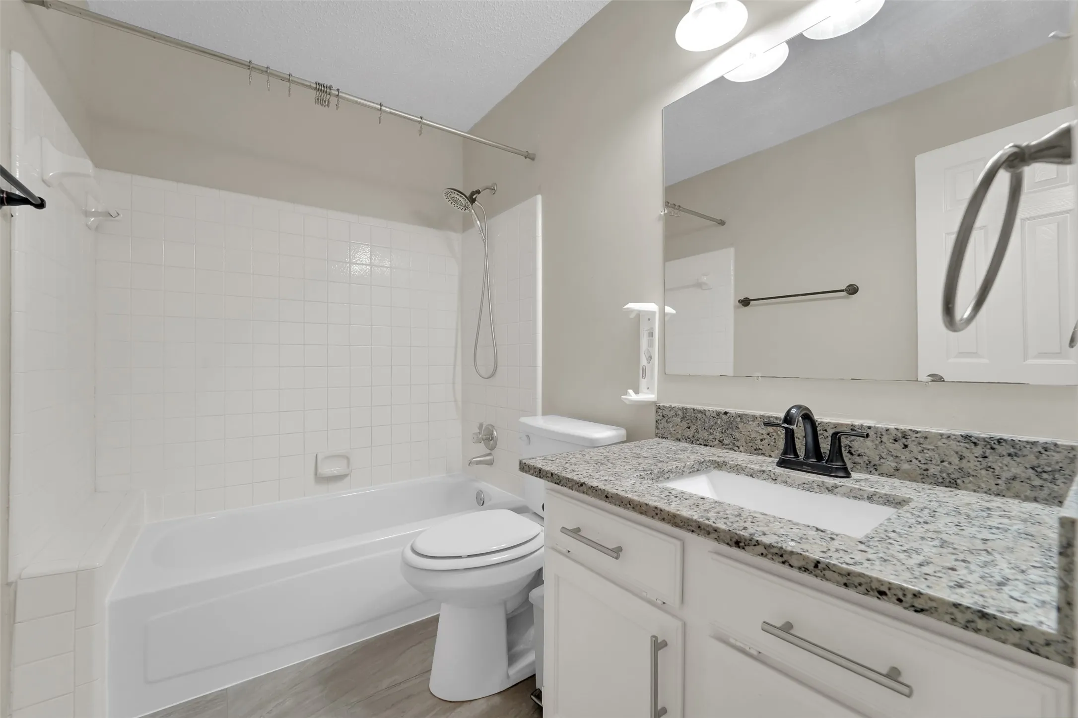 Modern bathroom featuring a white subway tile shower surround with frameless glass enclosure, dual-sink vanity with polished stone countertop, wood-finish flooring, and contemporary matte black hardware and fixtures throughout