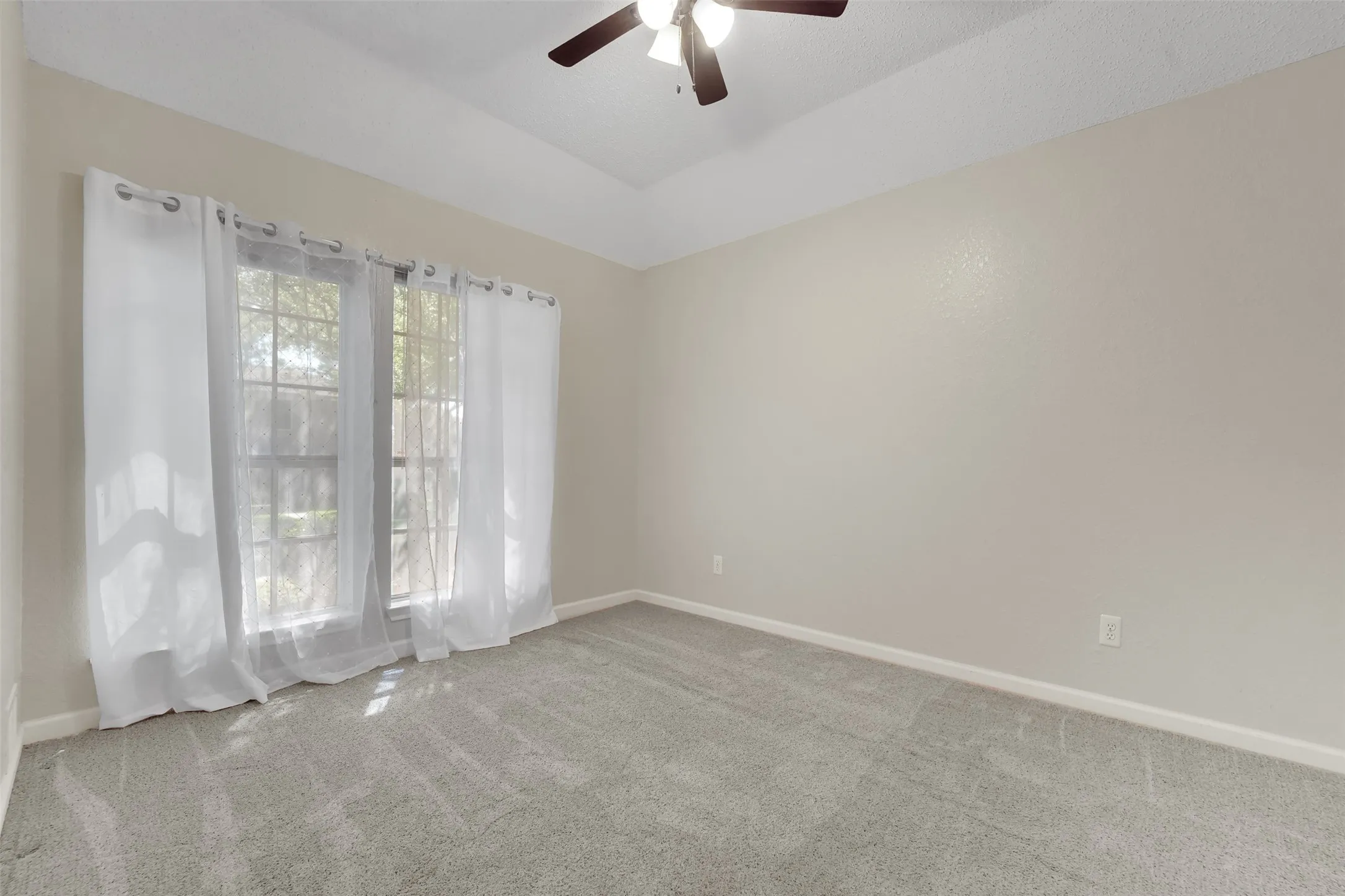 Vaulted ceiling with a ceiling fan, dual windows, neutral wall paint, and grey carpet flooring