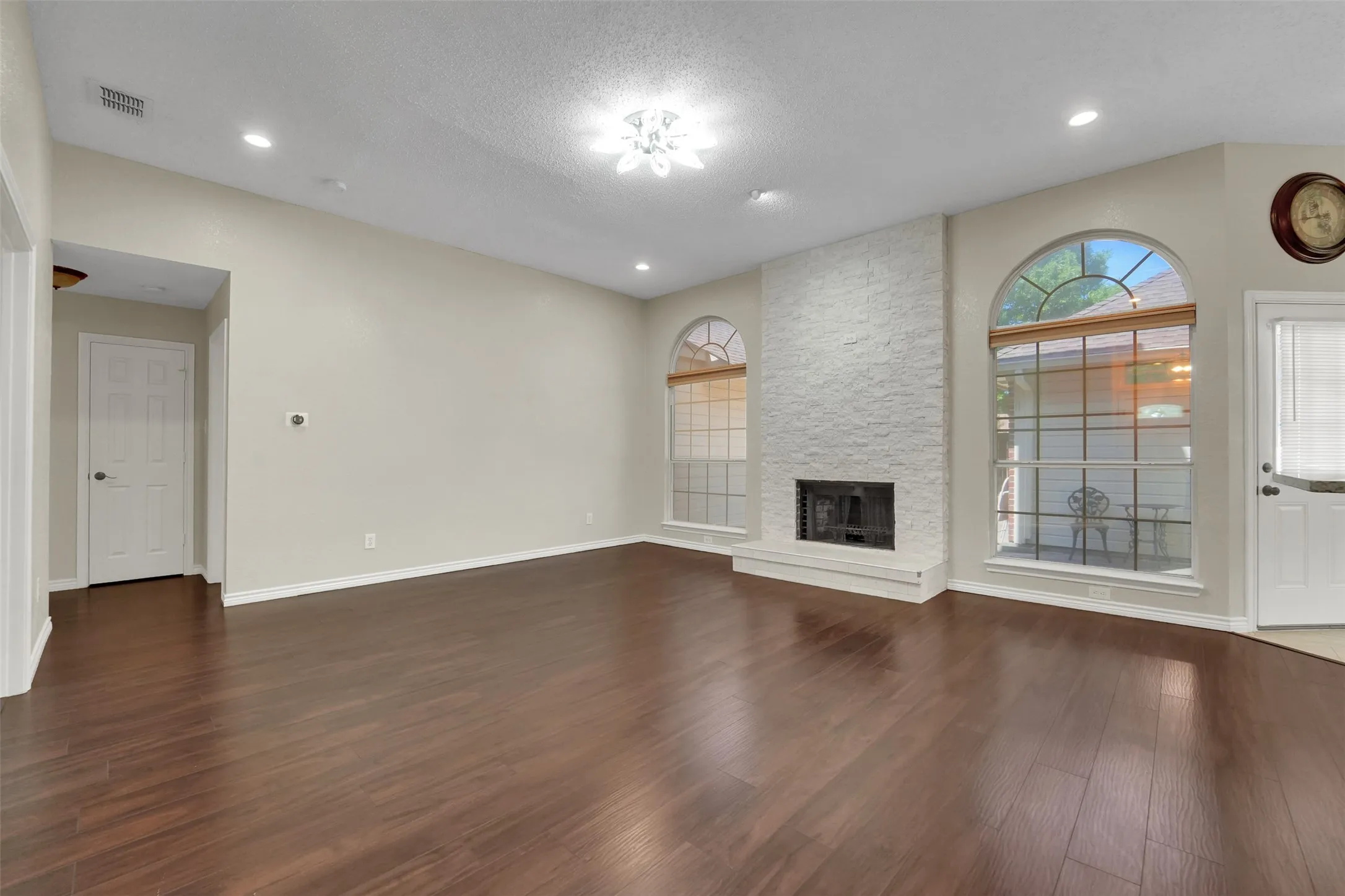 Spacious open-concept living area featuring rich wood-finish flooring, recessed ceiling lighting, and a striking brick fireplace with arched transom​​‌​​​​‌​​‌‌​‌‌​​​‌‌​‌​‌​‌​​​‌​​ window