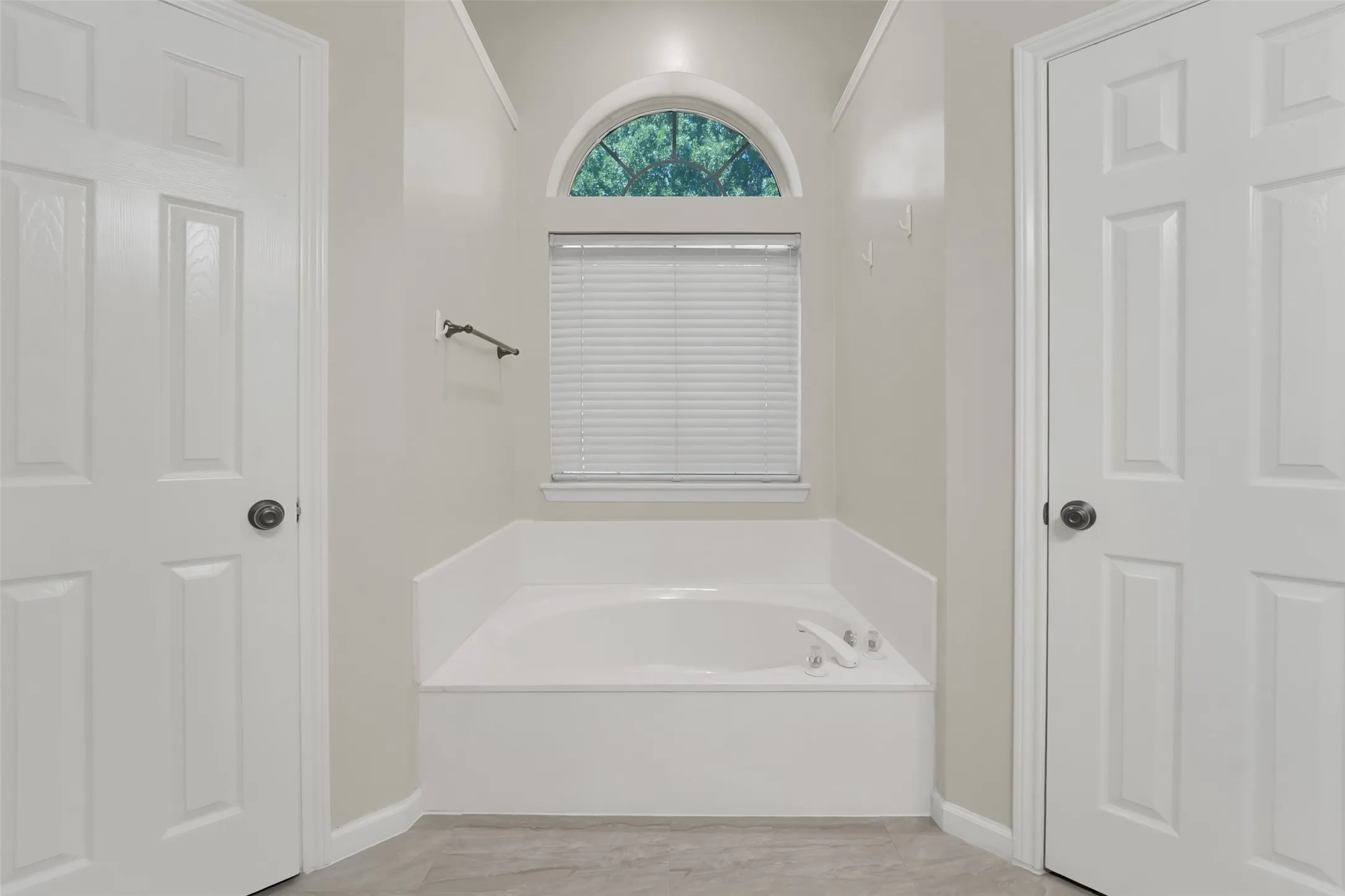 Primary Bathroom featuring a spacious soaking tub with integrated controls, ceramic tile surround, neutral finish flooring, dual six-panel closet doors, and a transom window with operable shutters providing natural light