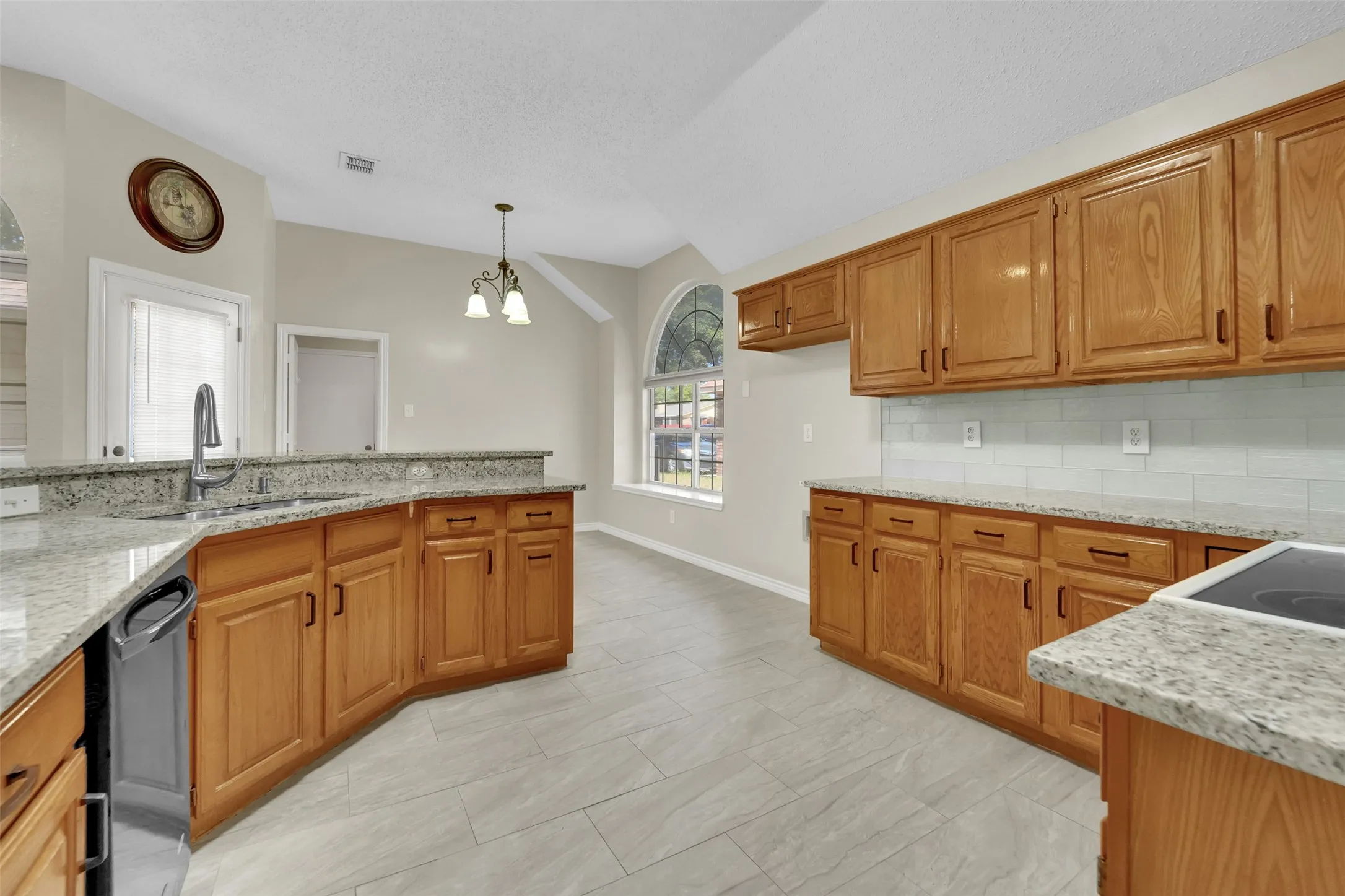 Spacious kitchen featuring warm wood cabinetry, granite countertops, stainless steel appliances, tile flooring, and abundant natural light from multiple windows