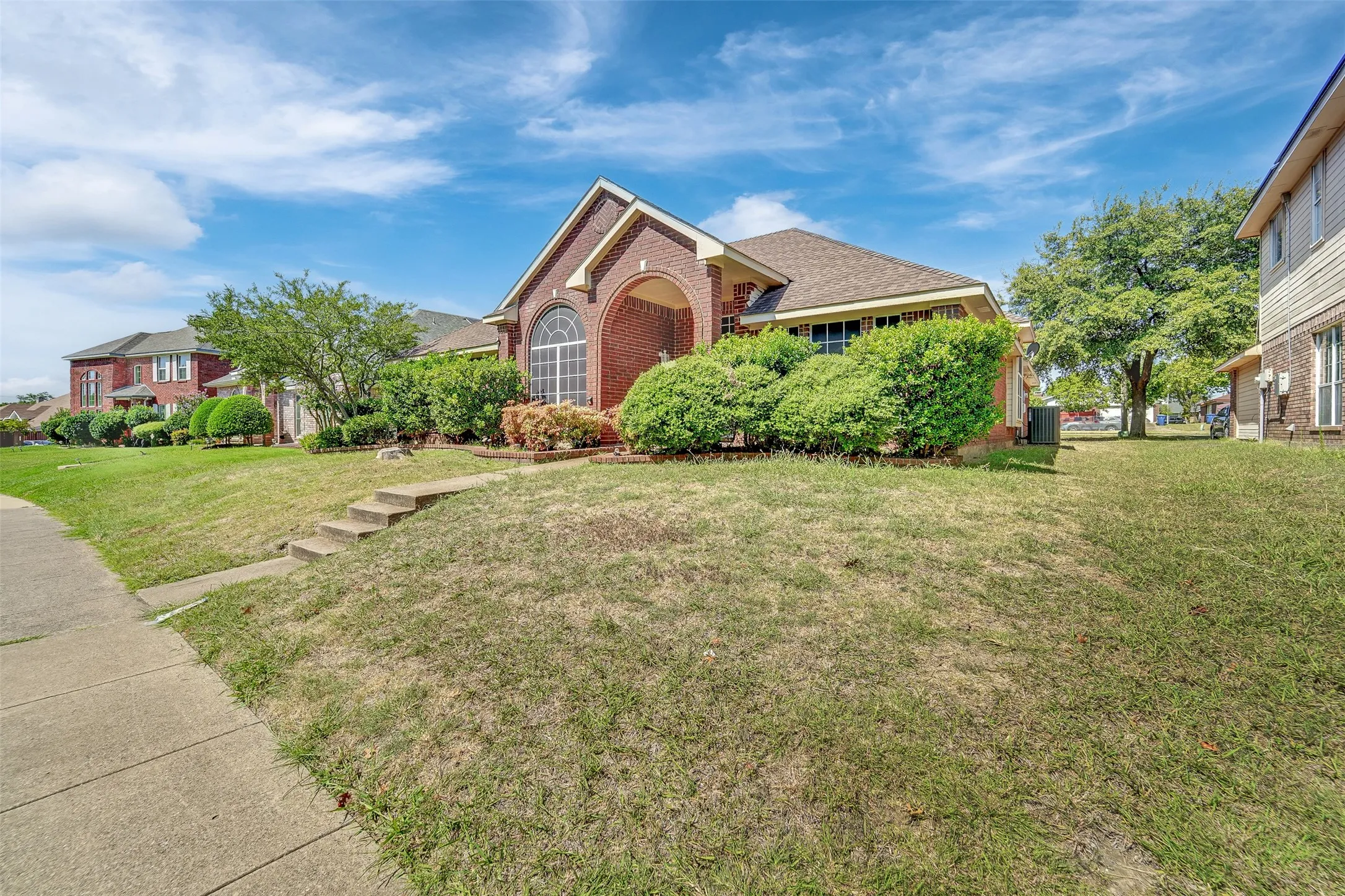 Brick exterior with an arched entry, prominent arched window, and mature front landscaping