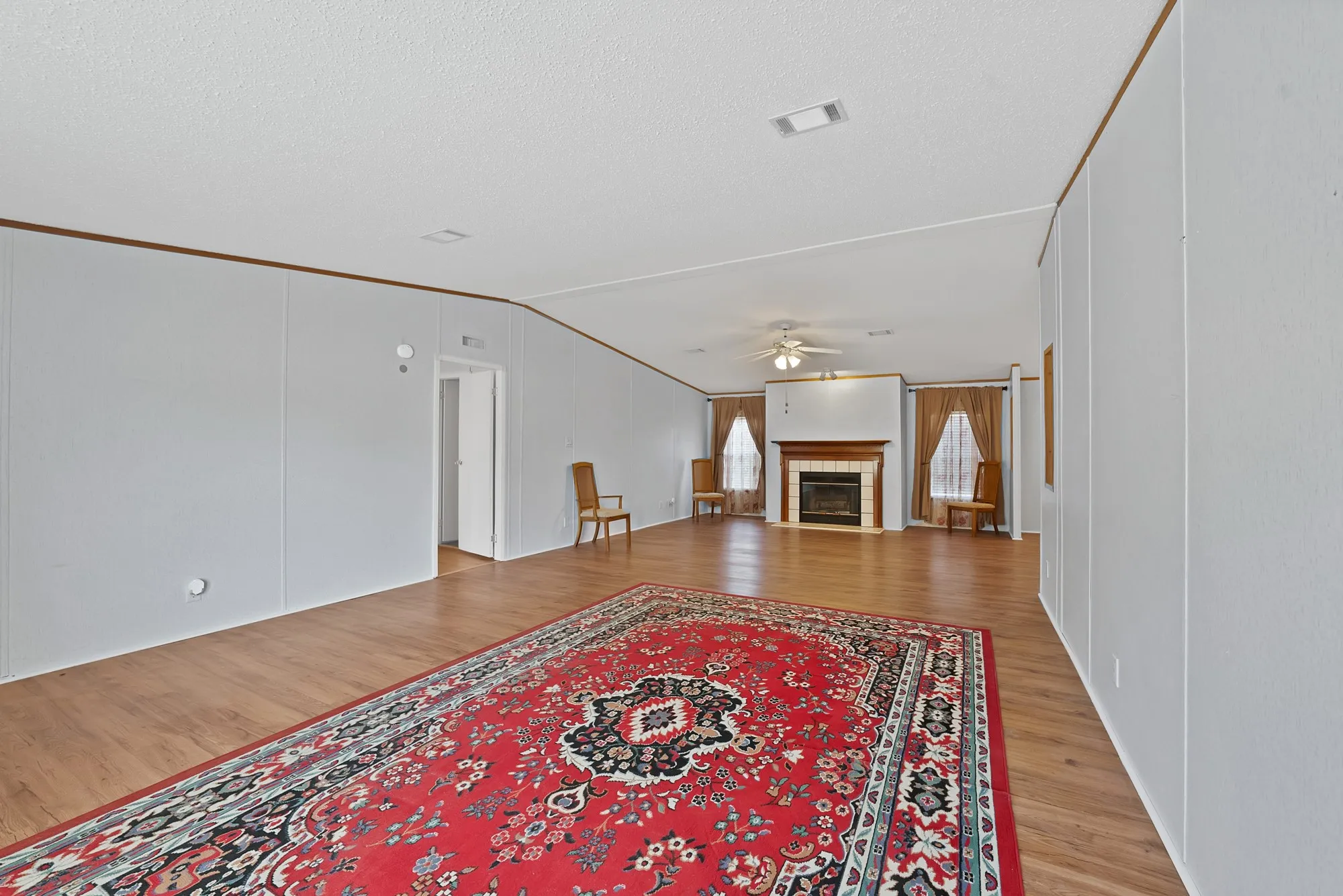 Spacious living area featuring wood-finish flooring, a fireplace with a wood mantle and tile surround, and a ceiling fan