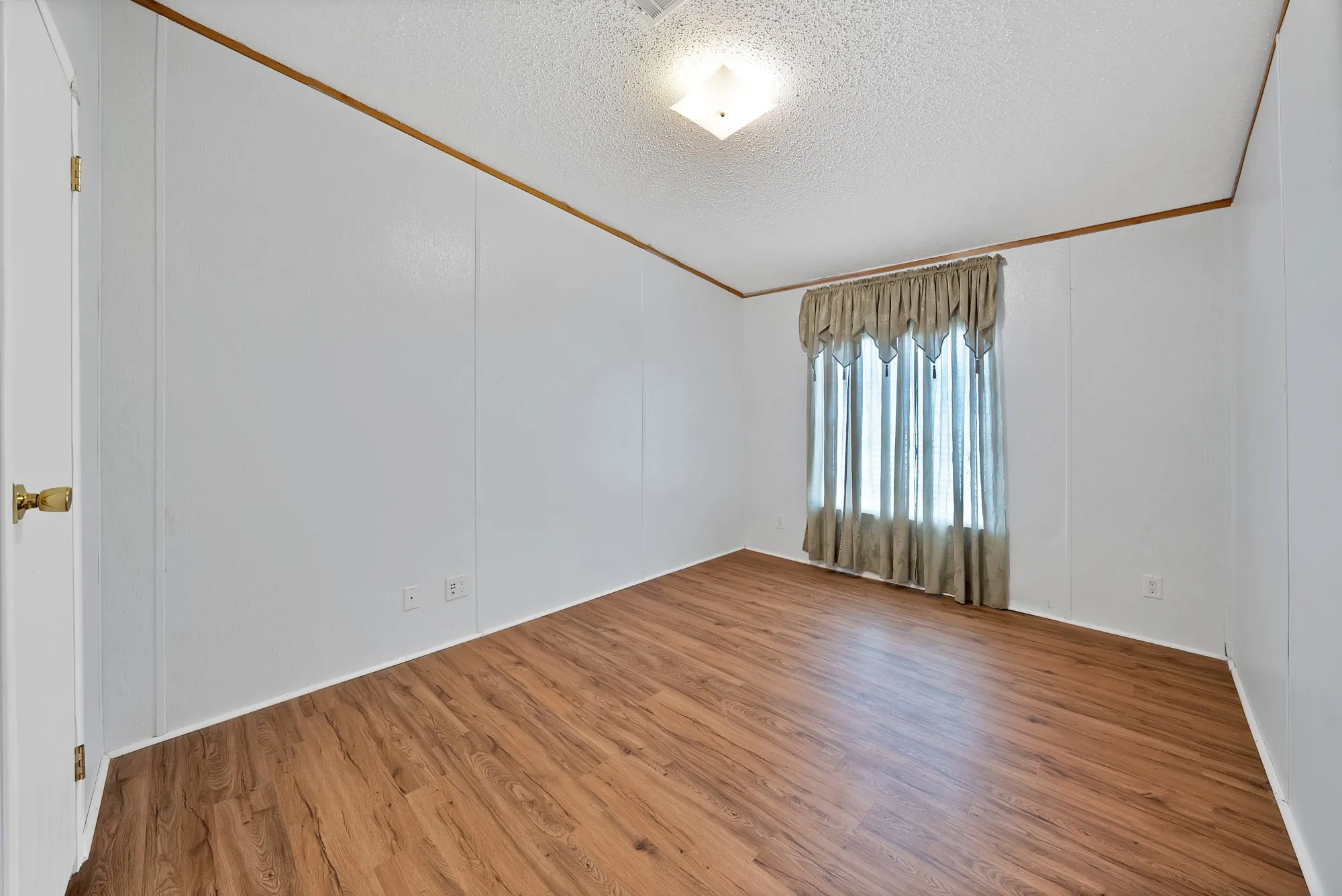 Wood-finish flooring, white paneled walls, and a window with drapes