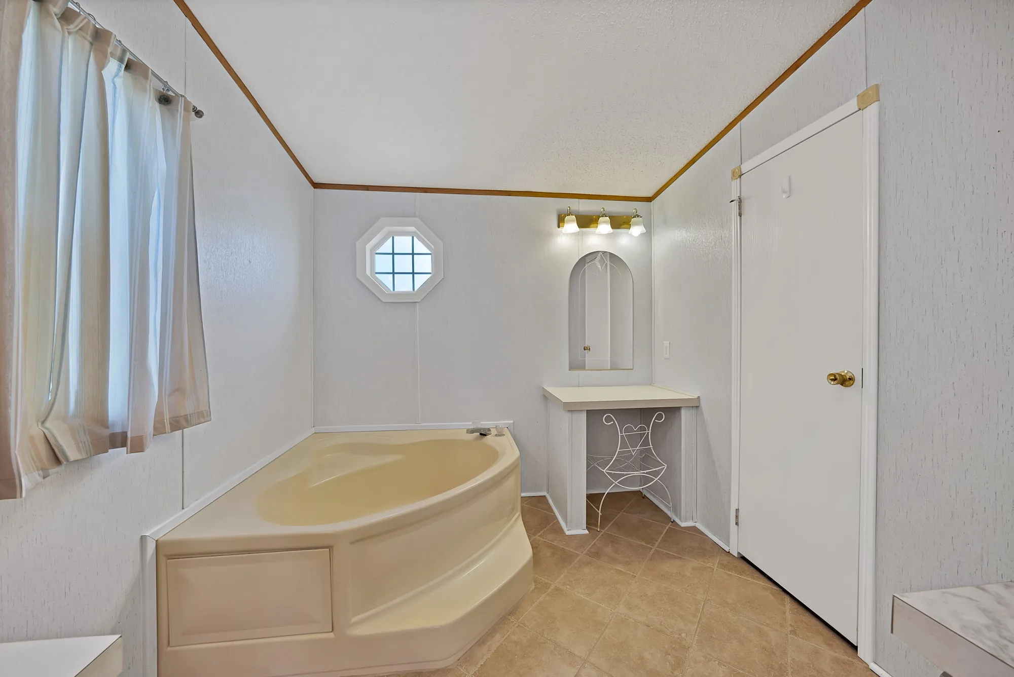 Corner soaking tub with integrated steps, octagonal window, vanity area with arched mirror, and tile flooring
