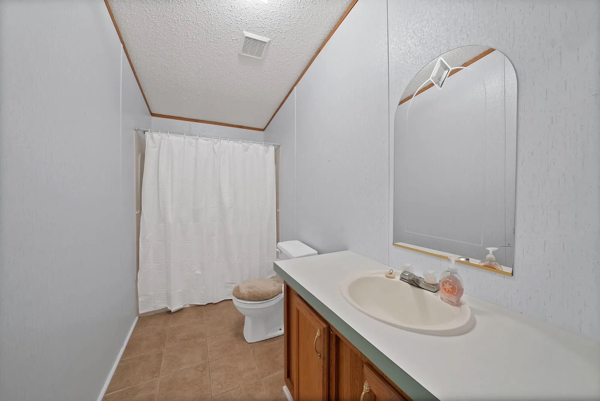 Integrated vanity with a single basin, tiled flooring, and an arched mirror