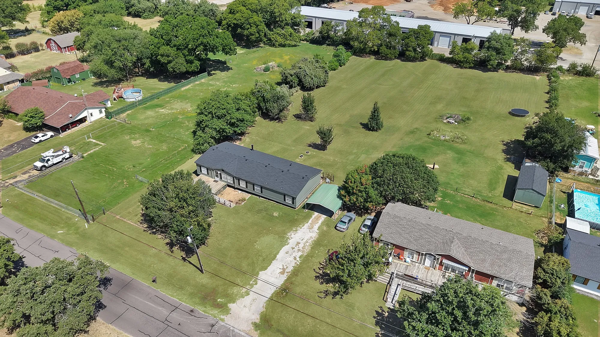 Expansive grassy lot with mature trees, paved driveway, and multiple outbuildings