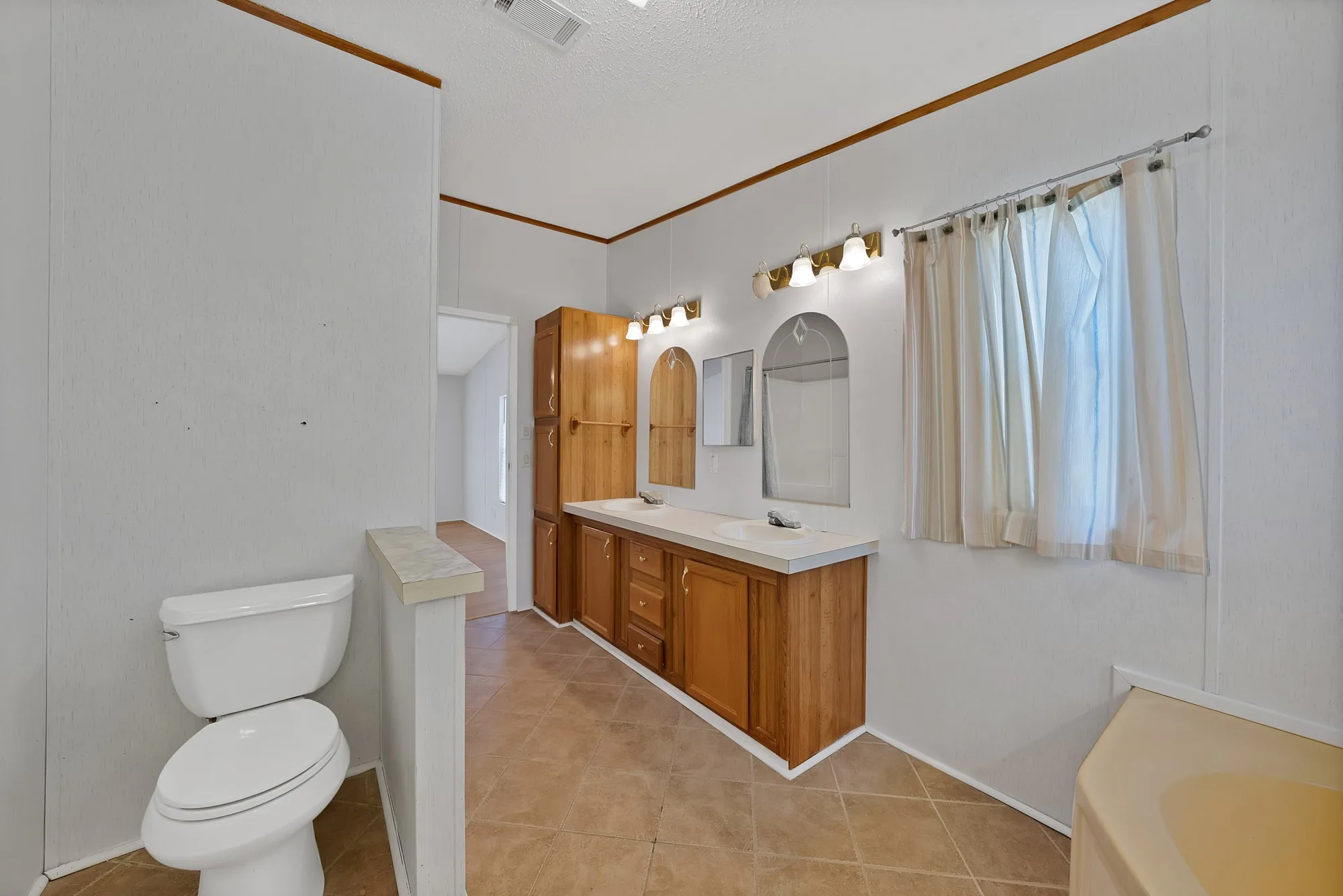 Dual vanity with wood-finish cabinetry, tile flooring, and a built-in tub