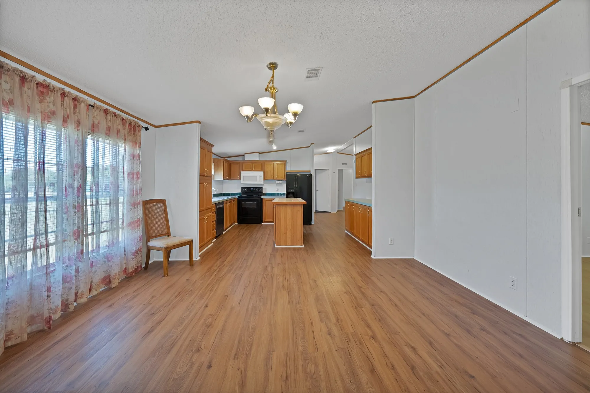 Wood-finish flooring throughout, with a kitchen featuring wood cabinetry, black appliances, and a central island
