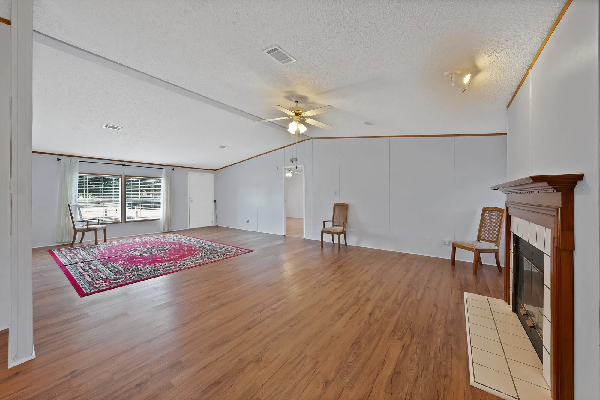 Expansive interior featuring wood-finish flooring, a built-in fireplace with a tile surround, large windows, and a ceiling fan