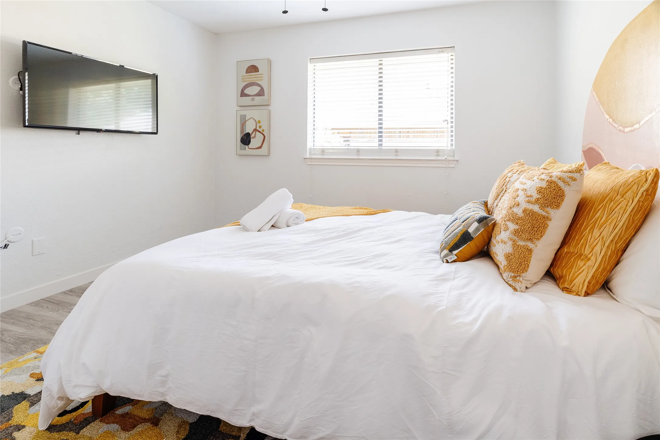 Wall-mounted television, window with blinds, and wood-finish flooring