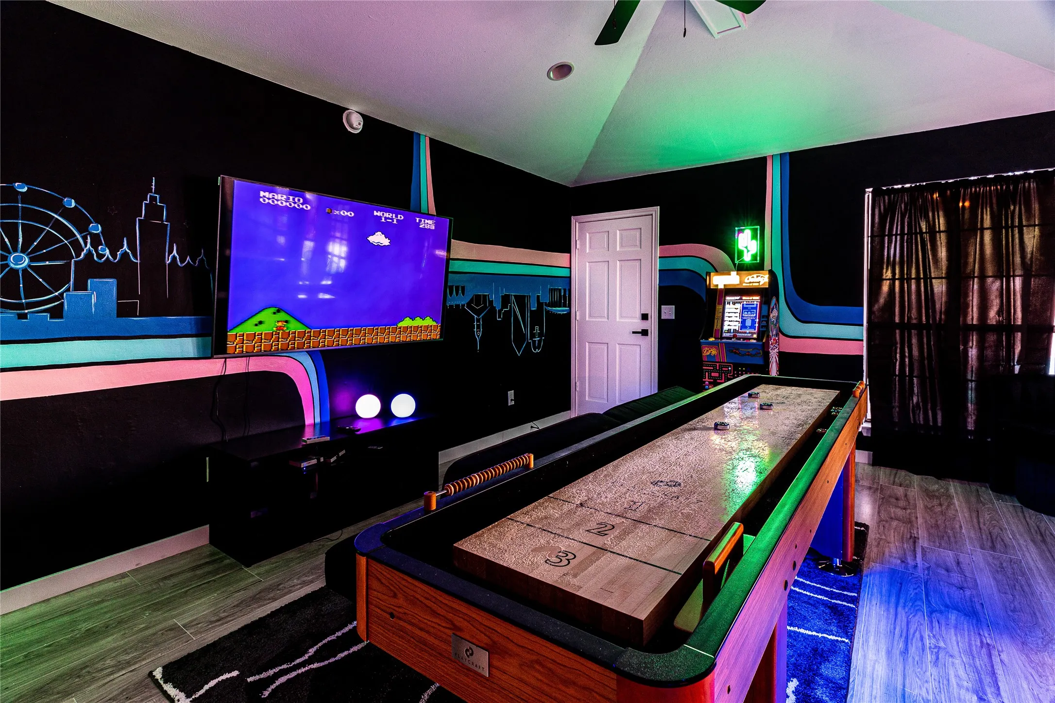 Shuffleboard table, mounted television, arcade game, ceiling fan, and wood-finish flooring