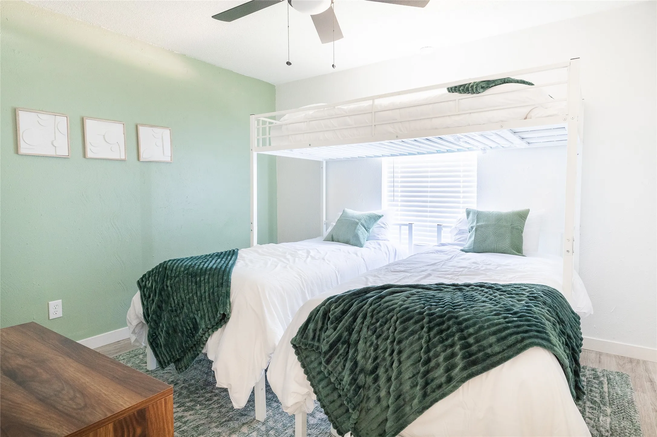 Light green accent wall, window with blinds, wood-finish flooring, and a ceiling fan