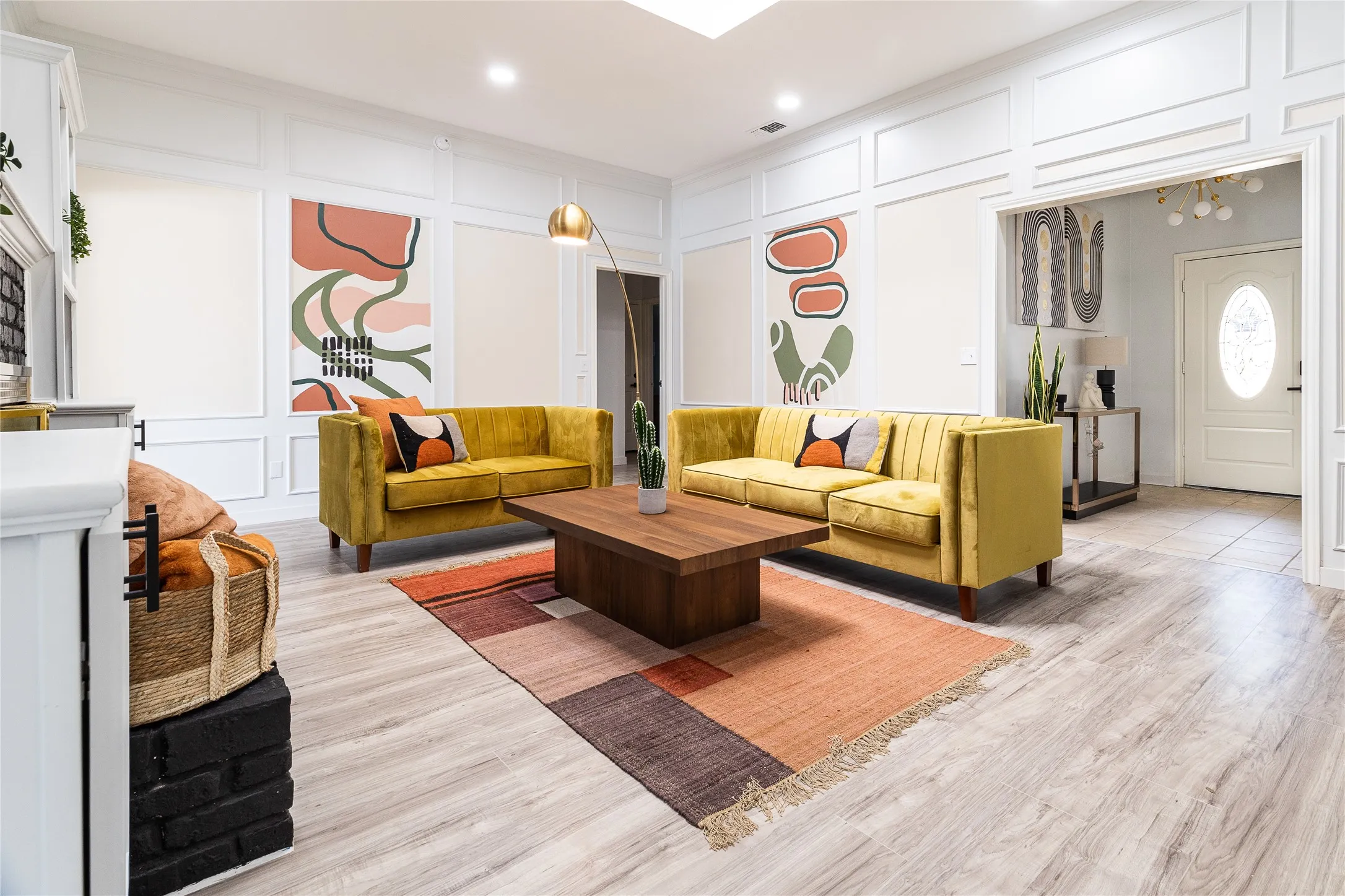 Light wood-finish flooring extending throughout, white paneled wall detailing, recessed lighting, and a white fireplace with a dark brick base