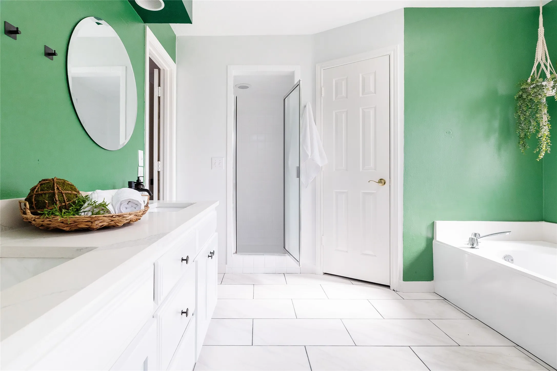 White tile flooring, spacious vanity with integrated sink, freestanding bathtub, and a glass-enclosed shower