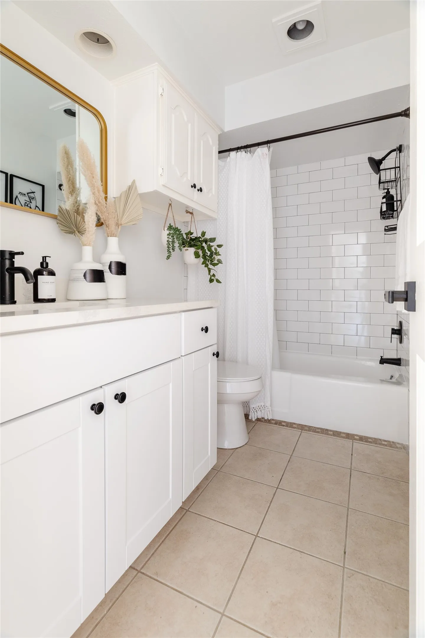 White vanity with matte black hardware, white subway tile shower surround, integrated white sink, bathtub with matte black fixtures, and beige floor tiling