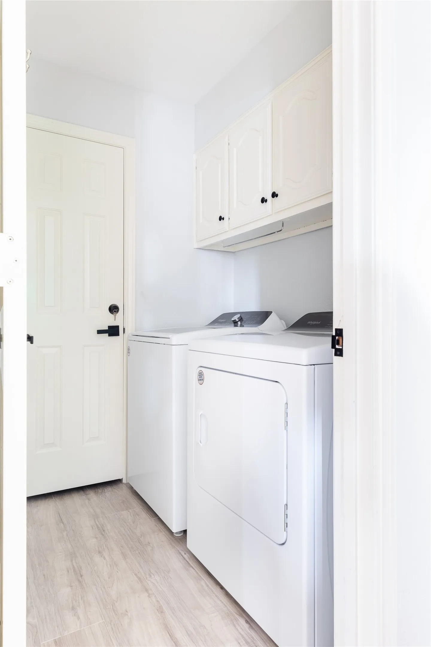 Laundry area featuring wood-finish flooring, white cabinetry, and white appliances