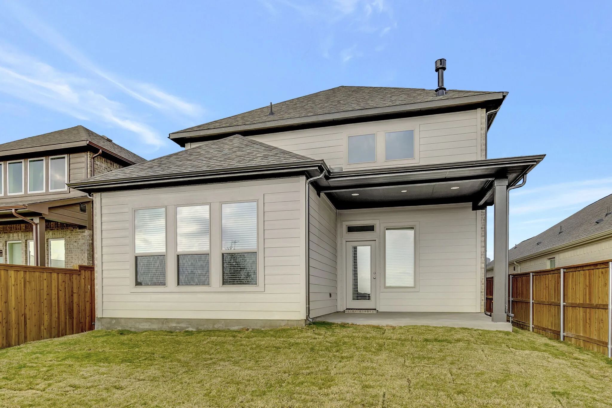 A covered patio overlooks the fenced, grassy back yard.