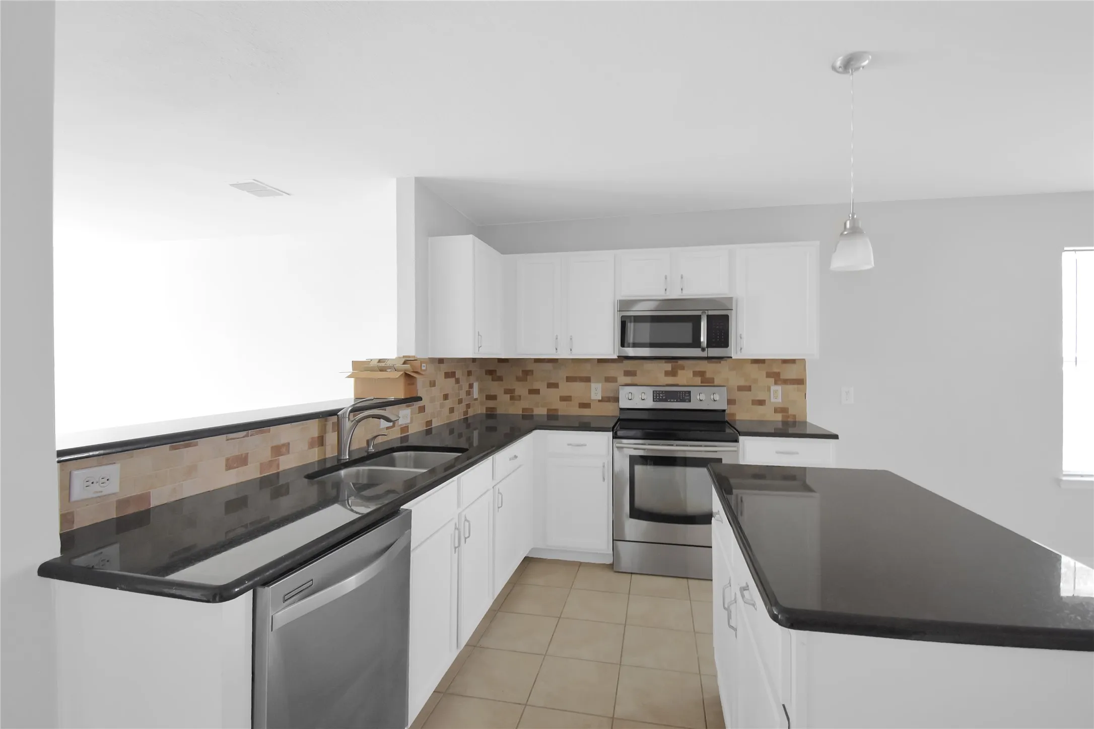 Modern kitchen featuring stainless steel appliances, including a gas range and microwave, paired with white cabinetry and a tiled backsplash