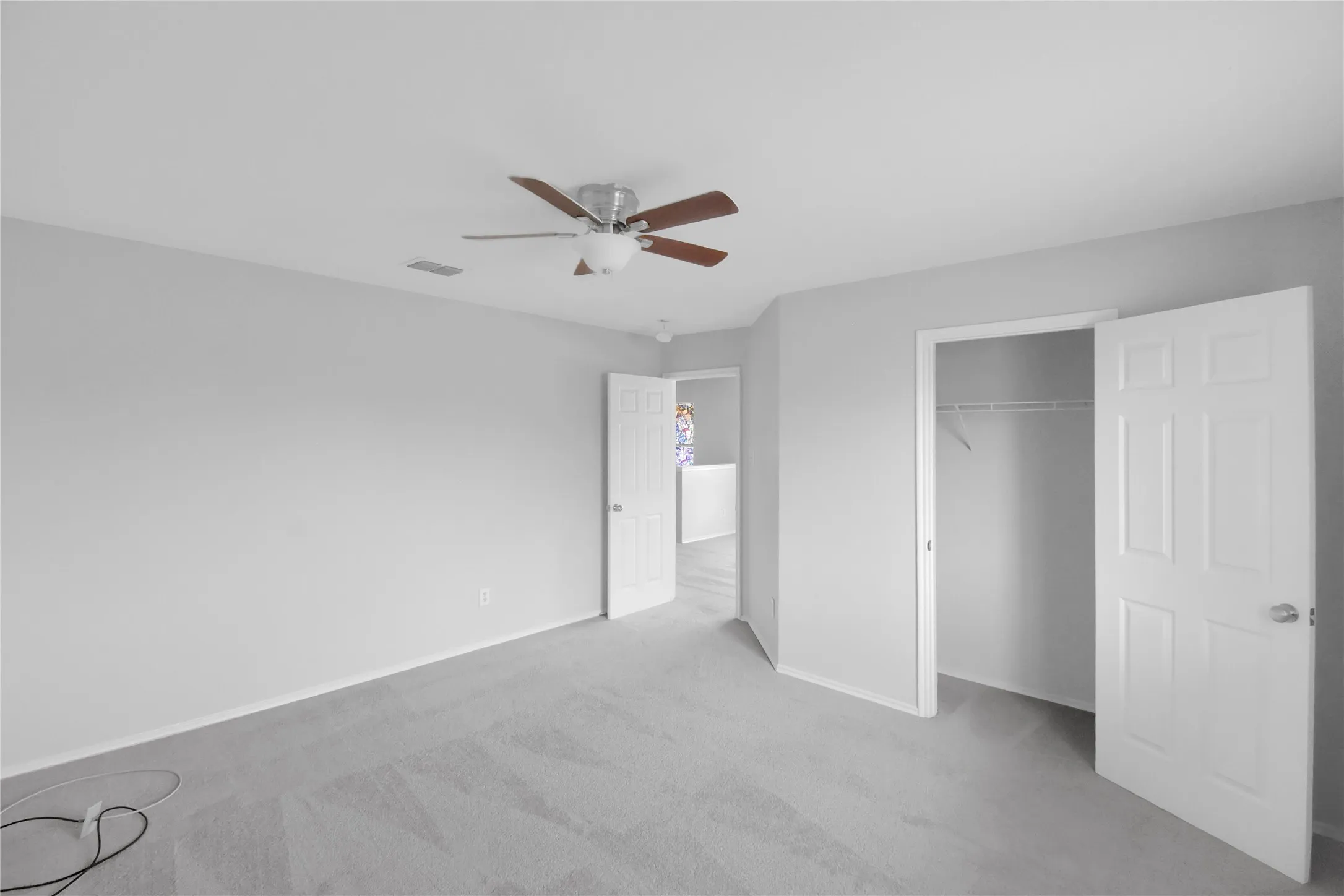 Spacious bedroom with neutral wall finishes, ceiling fan with integrated lighting, and dual closet entries providing ample storage