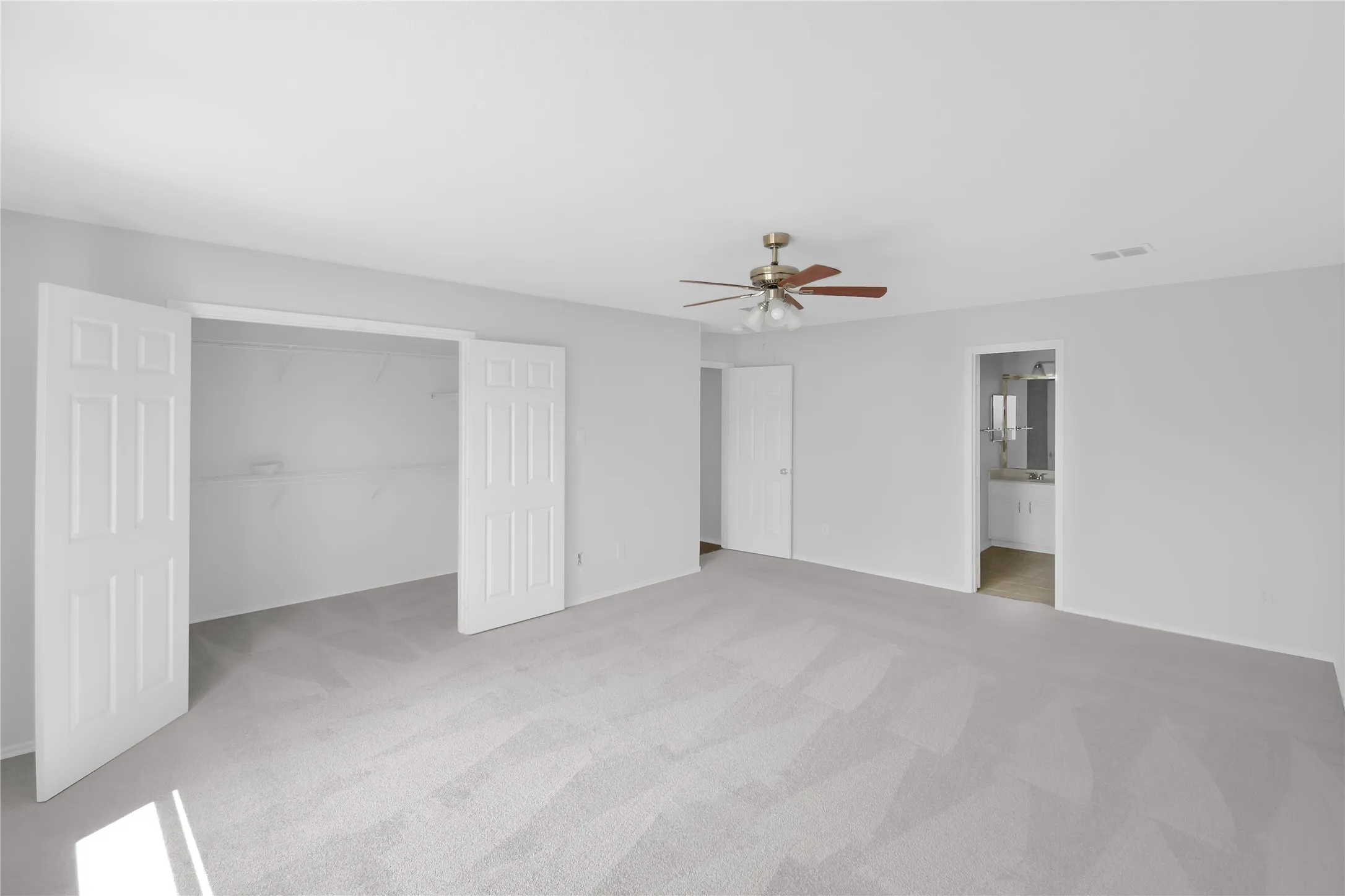 Spacious primary suite offering abundant natural light, multiple closet spaces with bifold doors, wood-finish flooring throughout, and a ceiling fan with brushed nickel finish