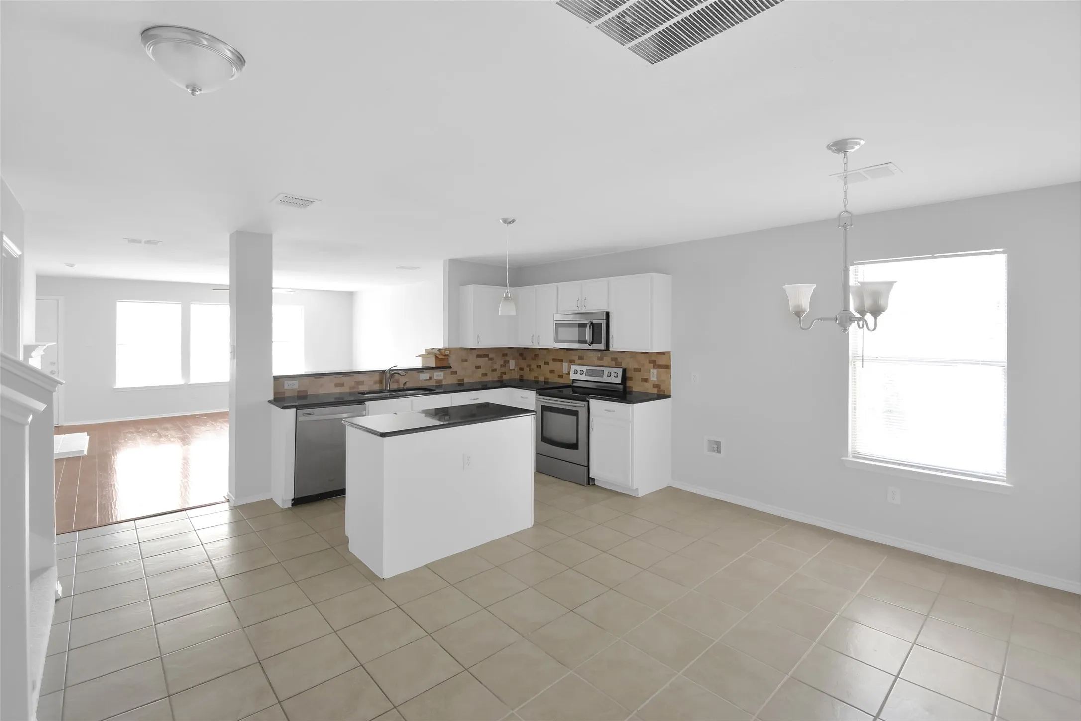 Spacious open-concept kitchen featuring a central island with wood-finish countertop, stainless steel appliances, white cabinetry, and tile flooring throughout
