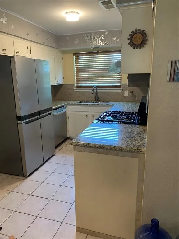 Kitchen featuring granite countertops, tile flooring, stainless steel appliances, white cabinetry, and a gas cooktop