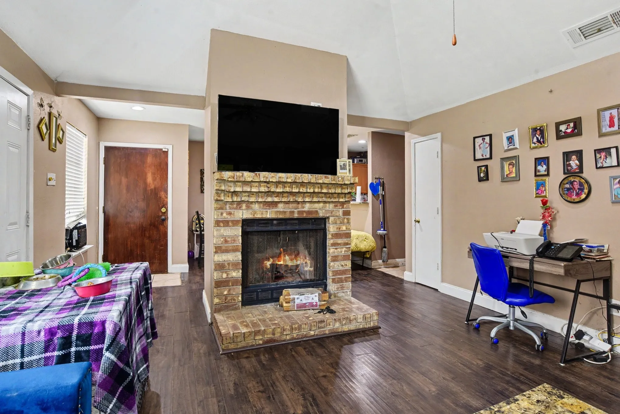 Spacious living area featuring a central brick fireplace feature, dark wood-look flooring, and ceiling fan.